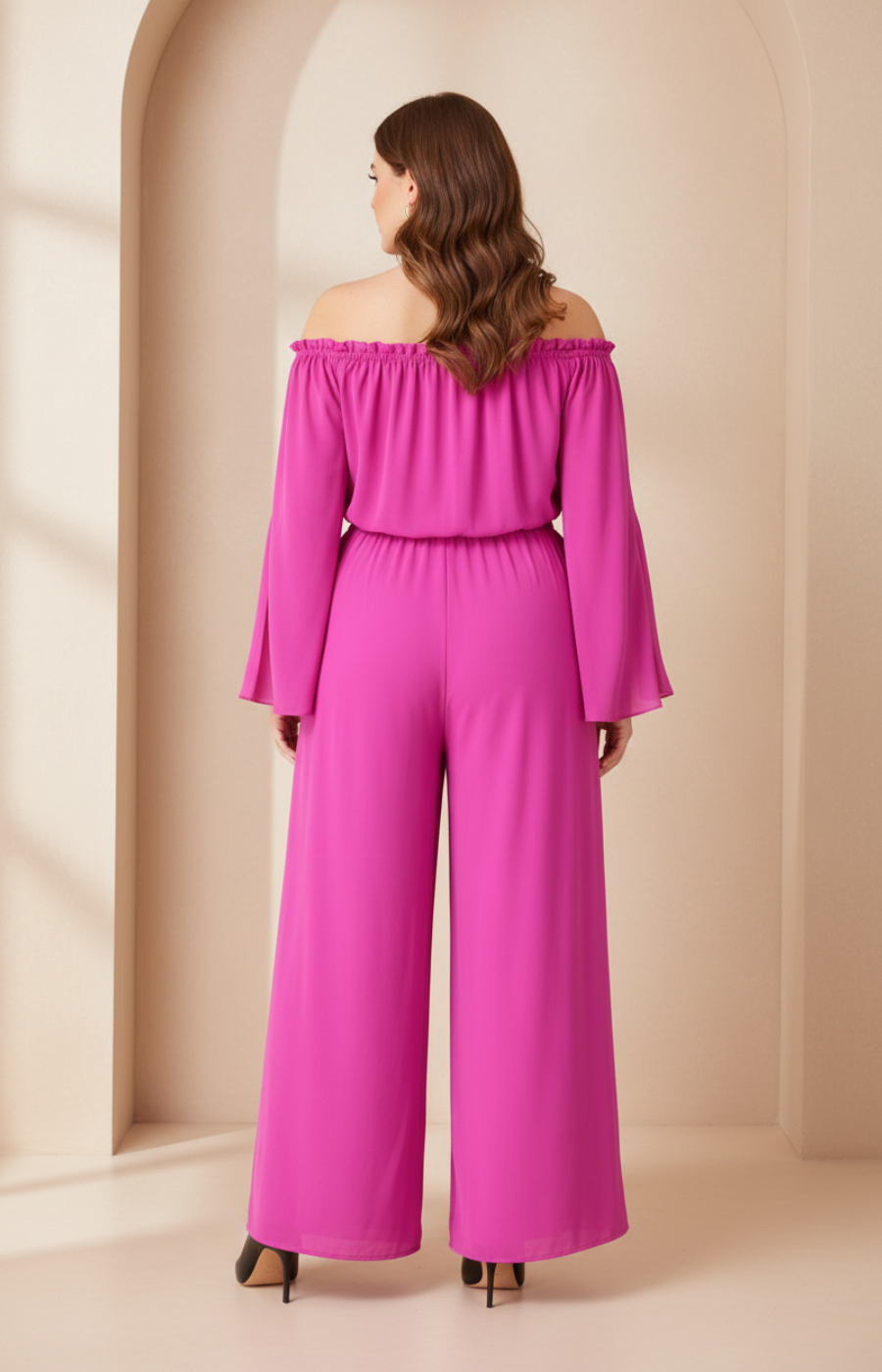 Woman wearing a pink off-shoulder jumpsuit in a beige room.