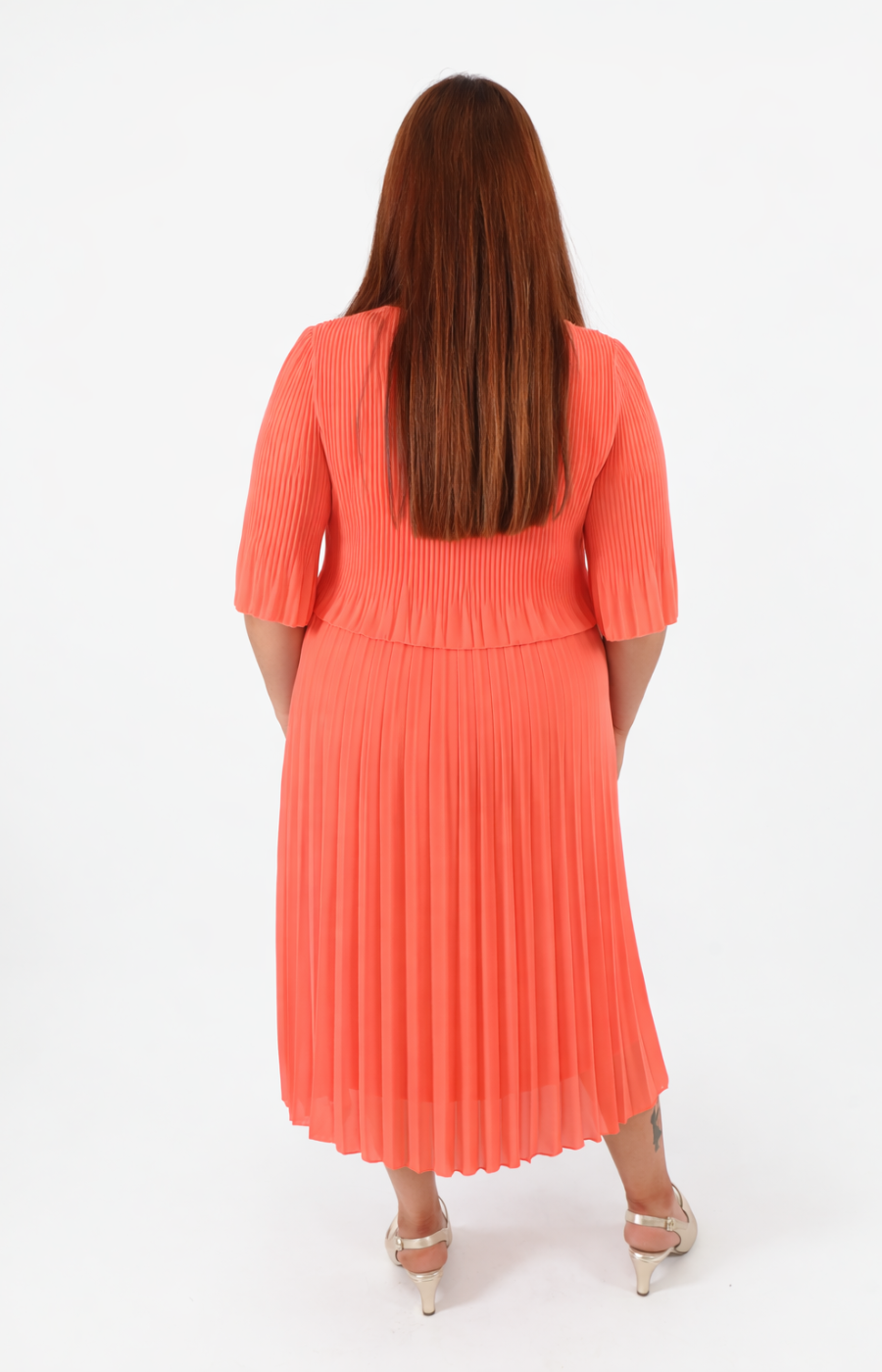 Woman wearing a coral pleated dress on a white background