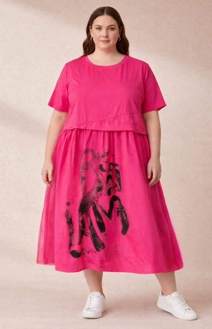 Woman wearing the bright pink Gemma dress with black abstract design, mesh netting to the side, soft, stretchy cotton top, on a beige background