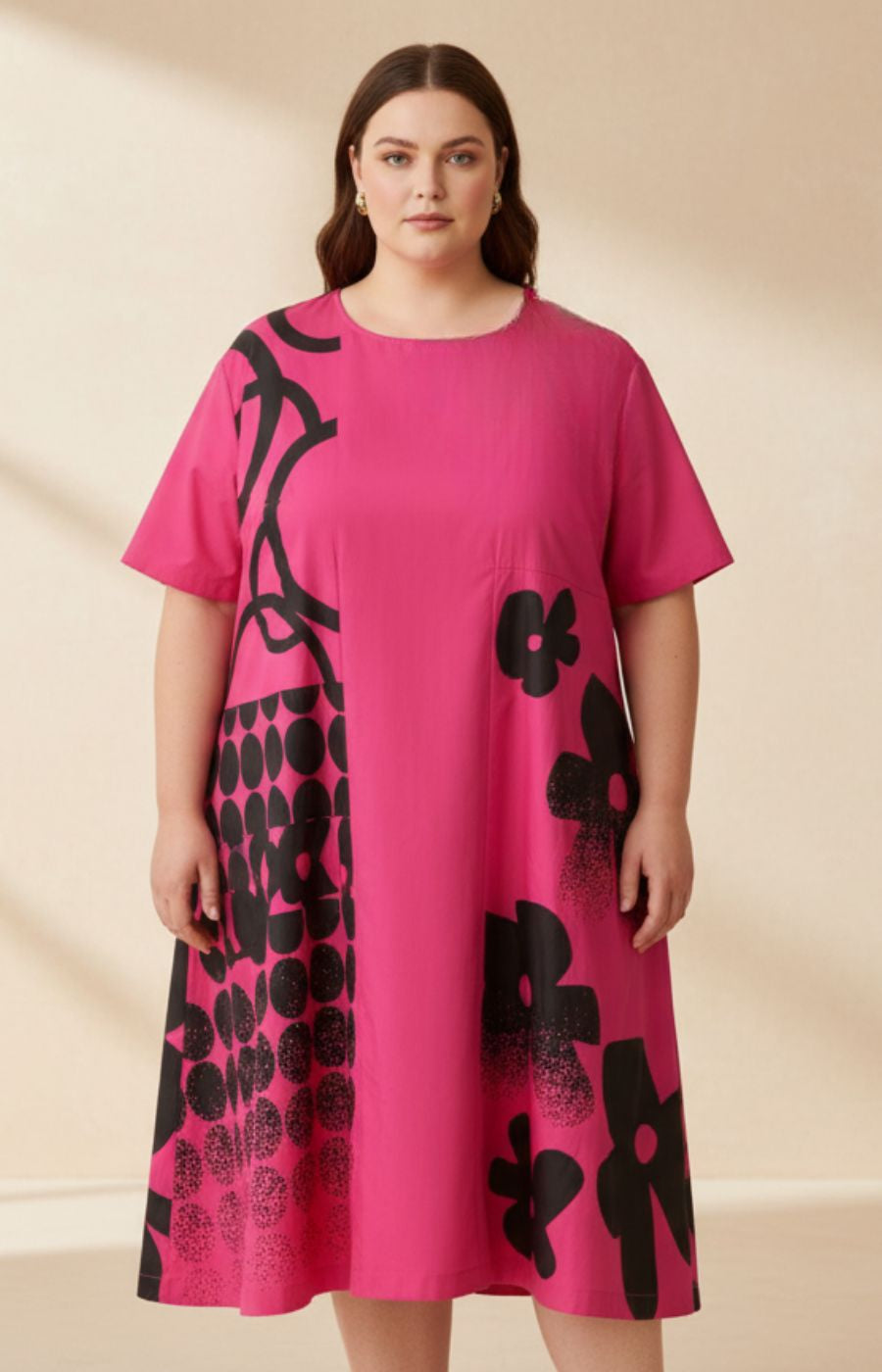 Woman wearing an A-line pink dress with short sleeves, a round neckline, pockets to the sides and black floral patterns on a beige background