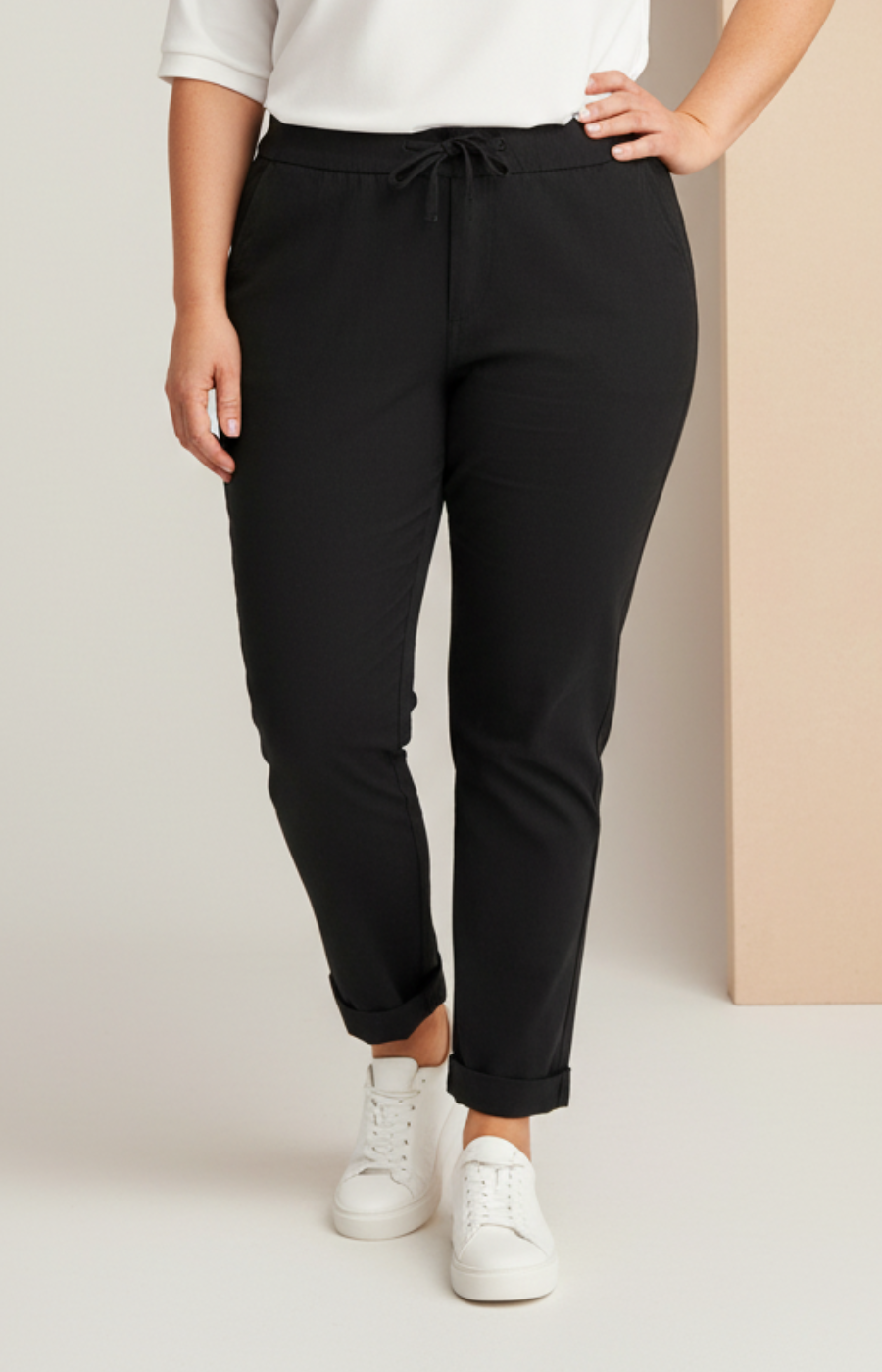 Person wearing black pants and white sneakers on a plain background