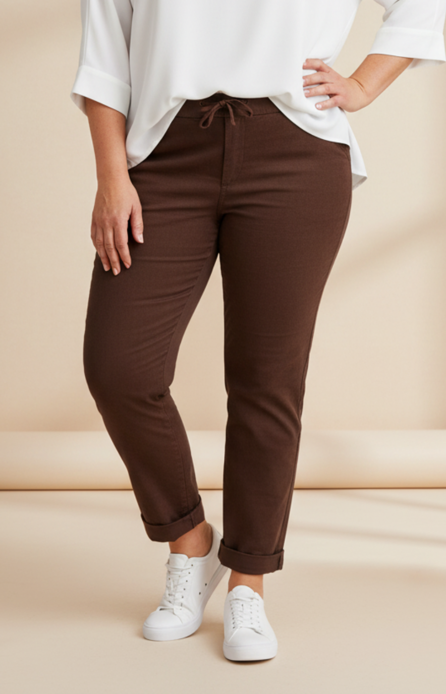 Person wearing brown pants and white sneakers on a beige background