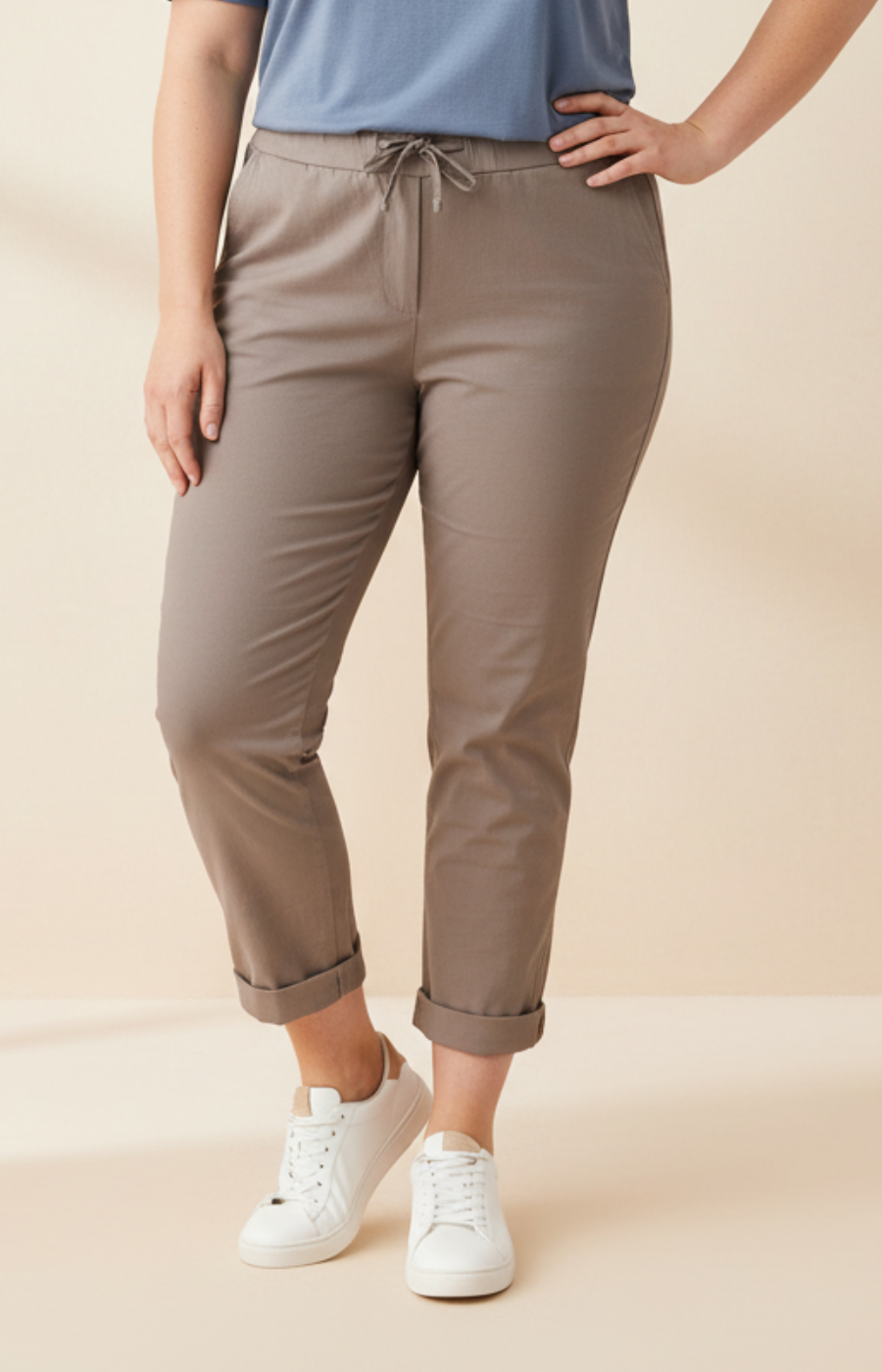 Woman wearing a blue t-shirt and taupe pants on a beige background