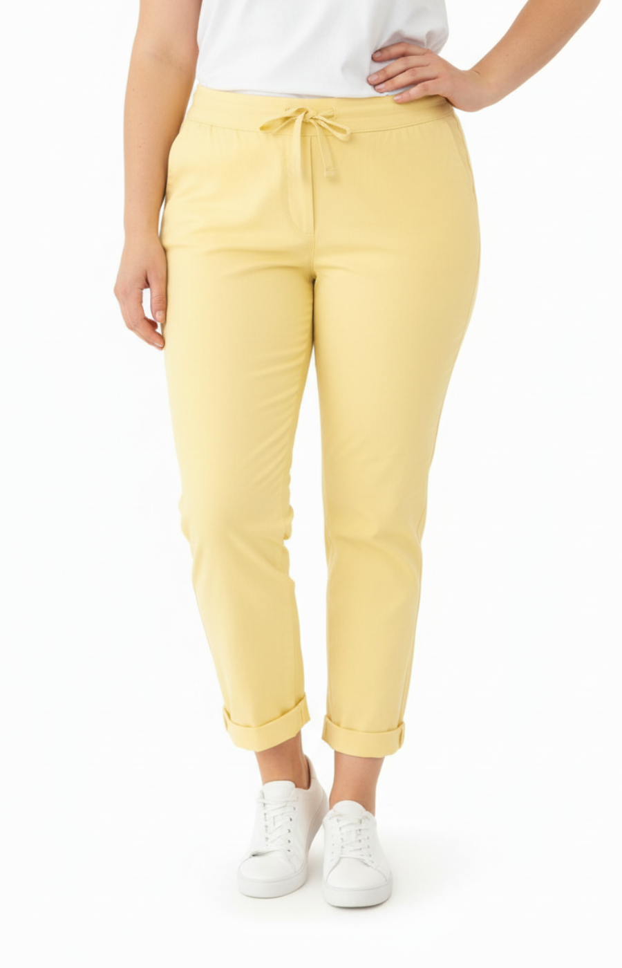 A curvy woman wearing yellow joggers and a white t-shirt on a white background