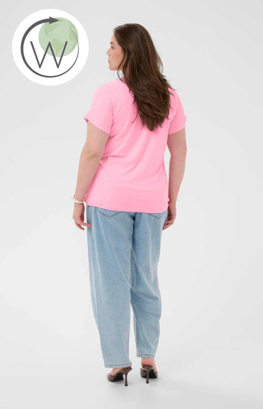Woman wearing a pink V neck t-shirt with short sleeves and elasticated hem and light blue pants on a white background