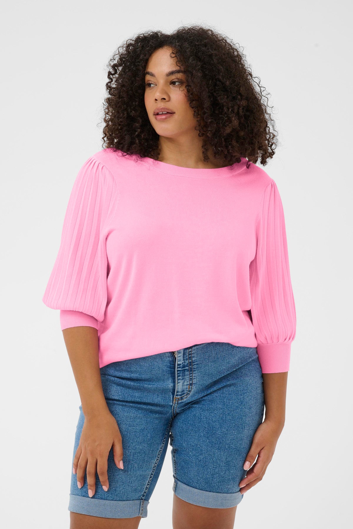 Woman wearing a pink knitted Loni top and blue denim shorts on a white background