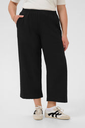 Person wearing black wide-leg culotte trousers and white sneakers on a white background
