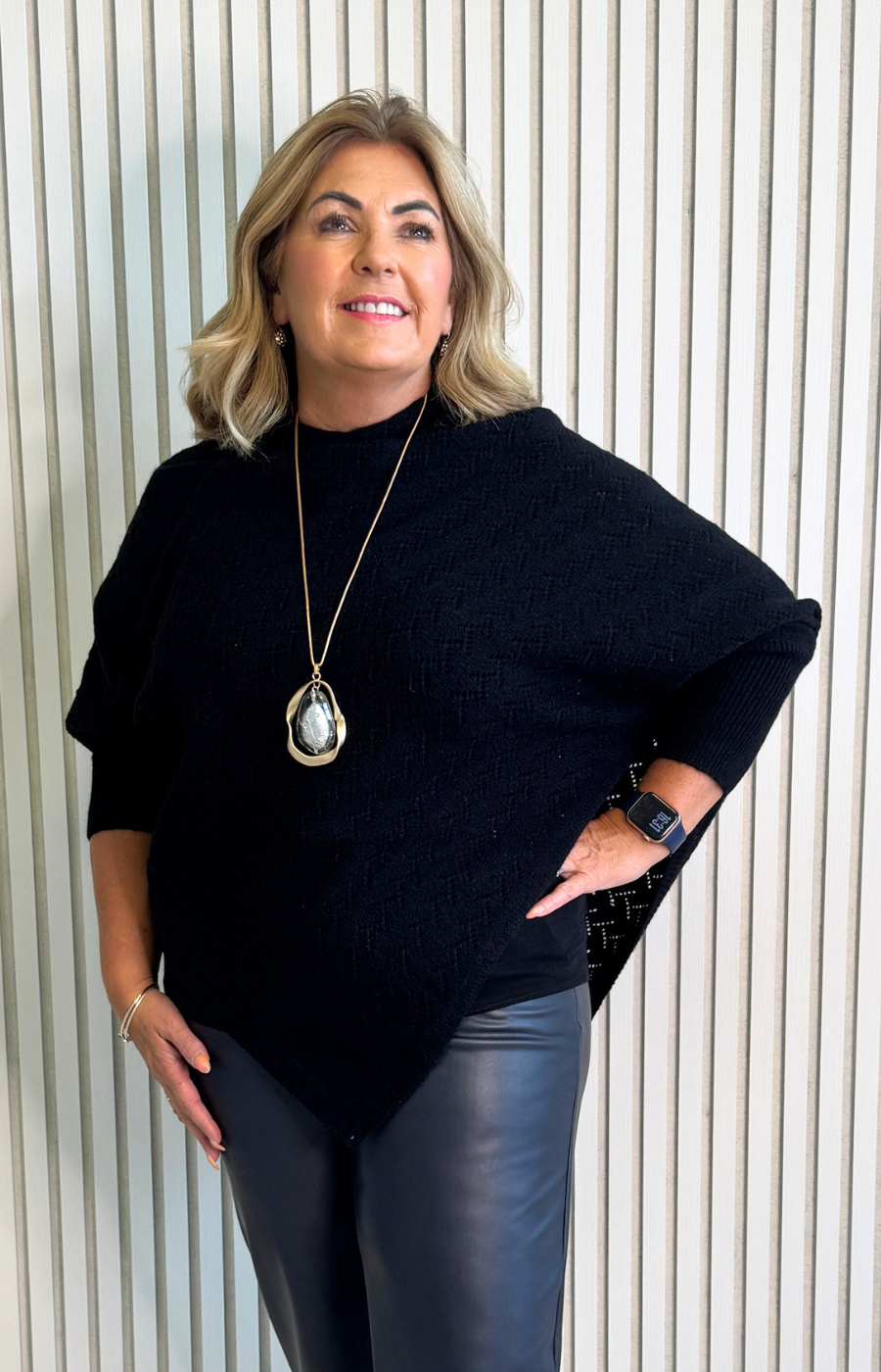 Woman wearing a black sweater and blue pants against a white wall