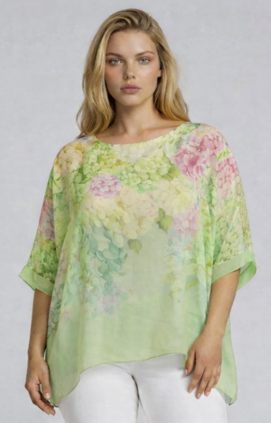 Woman wearing a light green floral blouse with a round neckline and 1/2 length sleeves against a plain background
