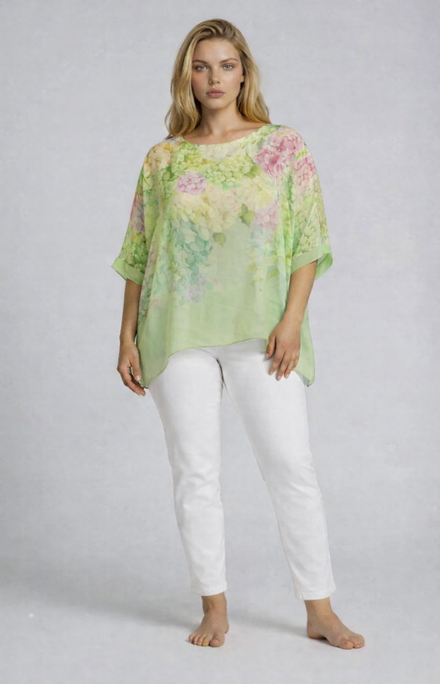 Woman wearing a light green floral blouse and white pants on a plain background