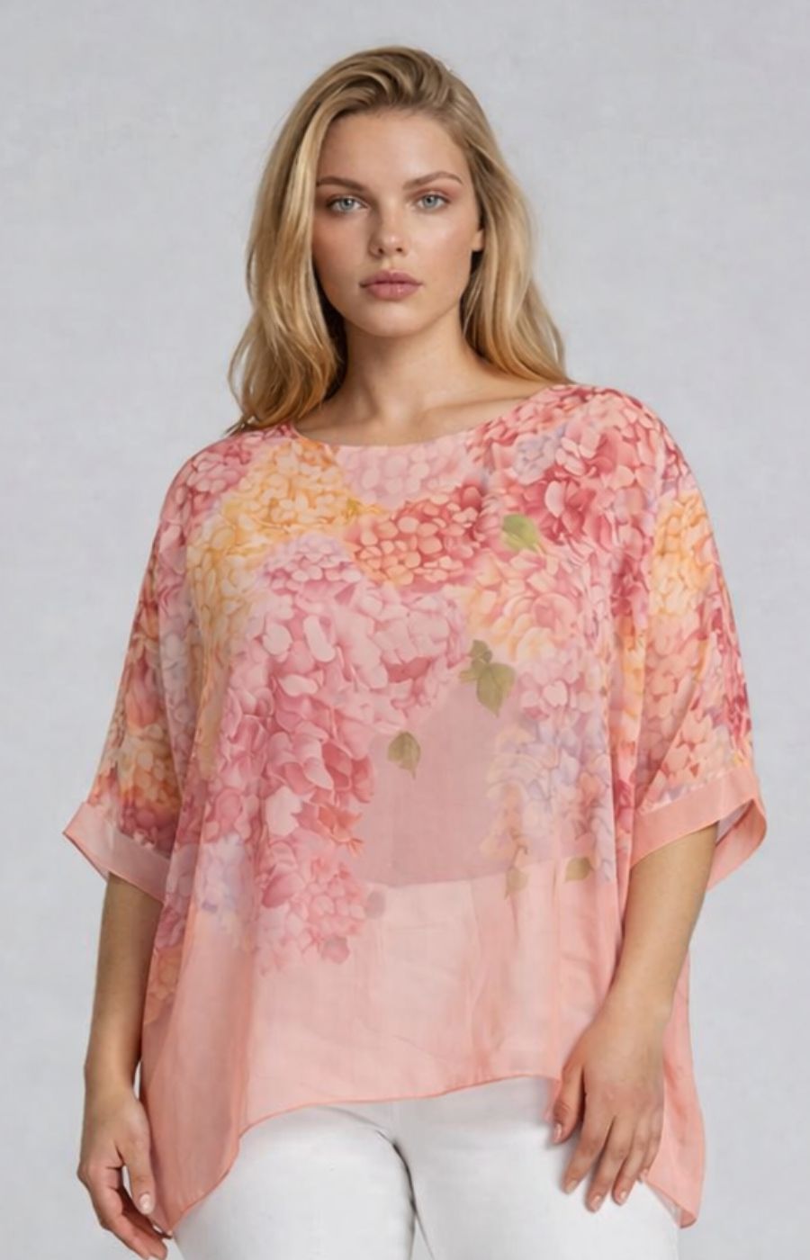 Woman wearing a pink chiffon blouse with a floral design and a round neckline and 1/2 length sleeves with a plain background