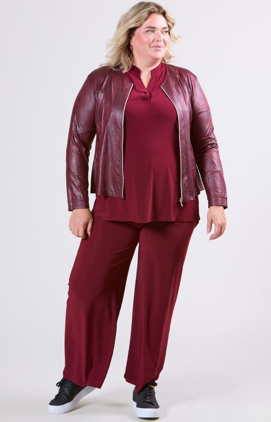 Woman wearing a burgundy leather jacket and matching pants on a white background