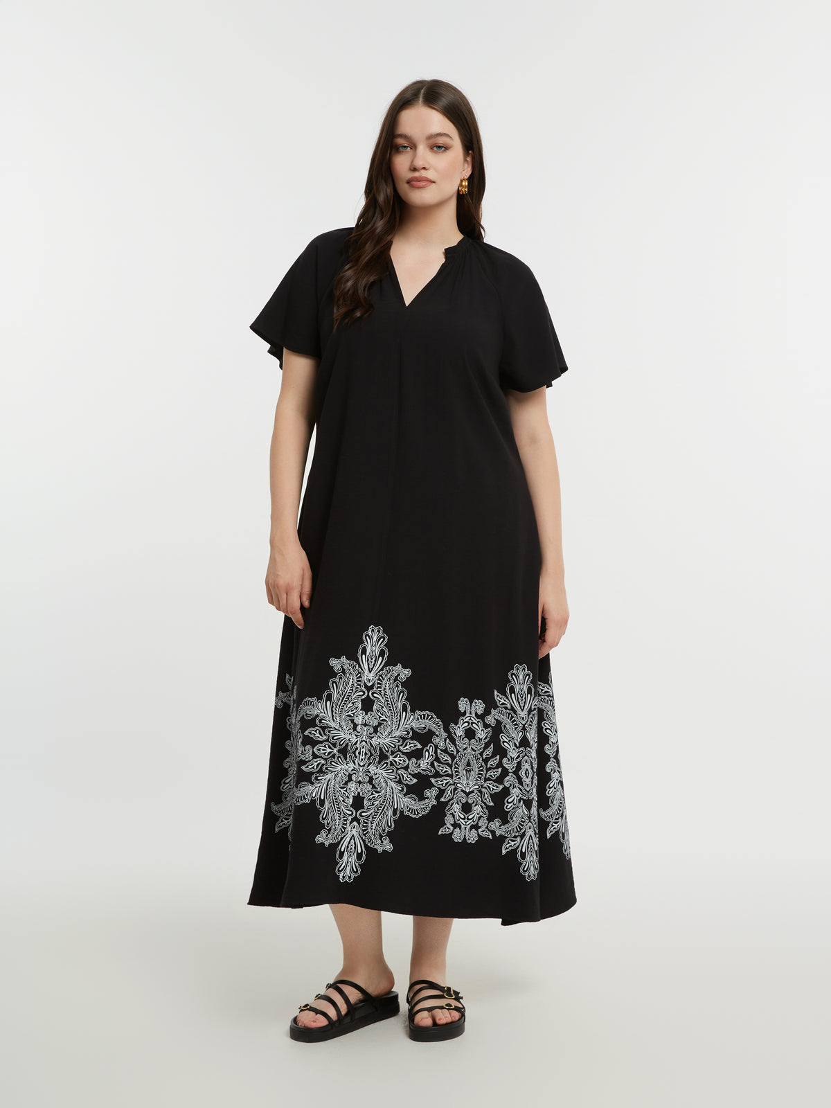 Woman wearing the Mat Black Dress with Paisley Print, a black midi dress with white embroidery, with an A-line shape, V neckline and short sleeves on a white background