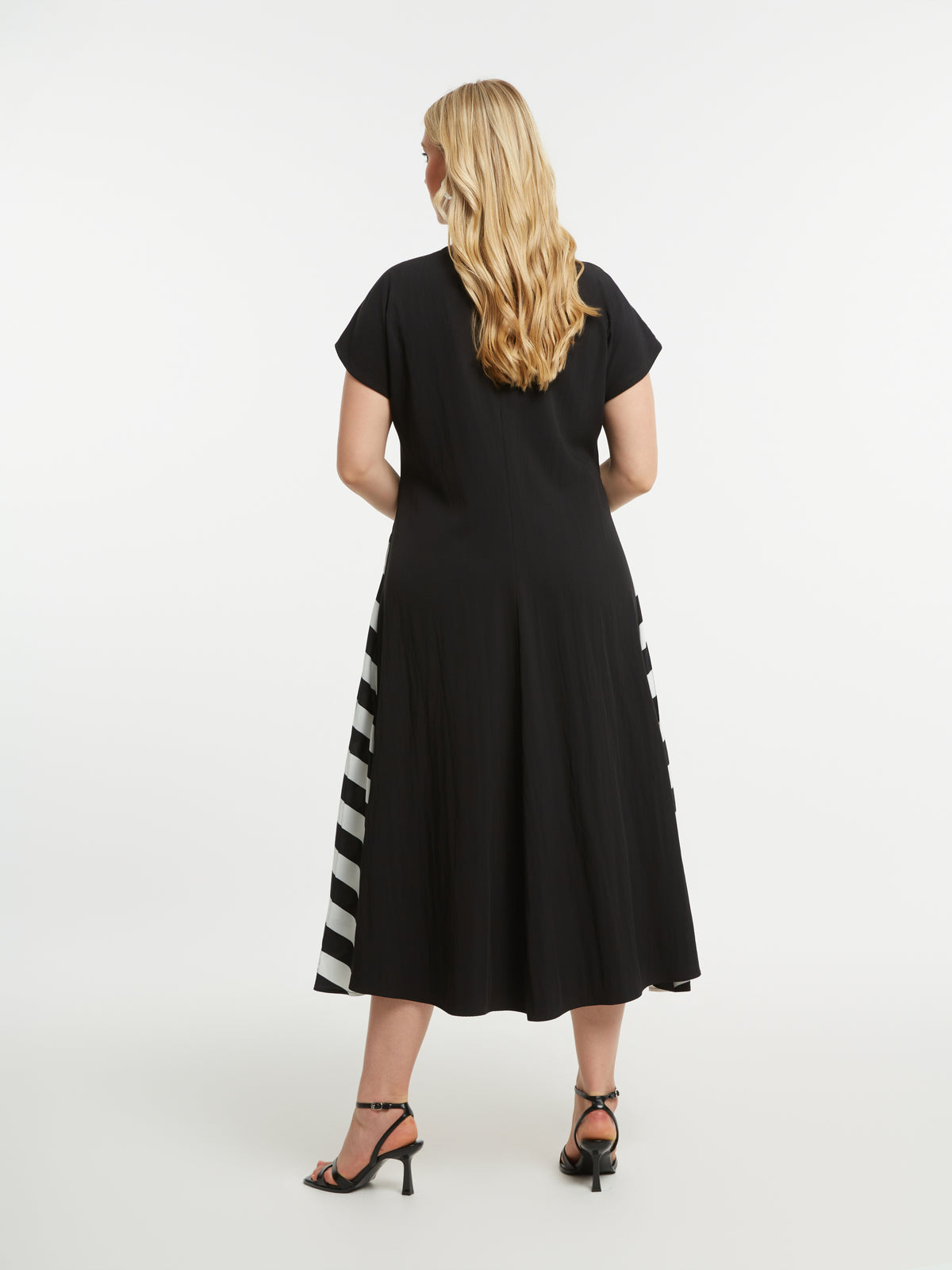 Woman wearing Mat Black Dress with Side Stripes, a black dress with a striped pattern on each side, a midi length, A-line dress with short sleeves on a white background