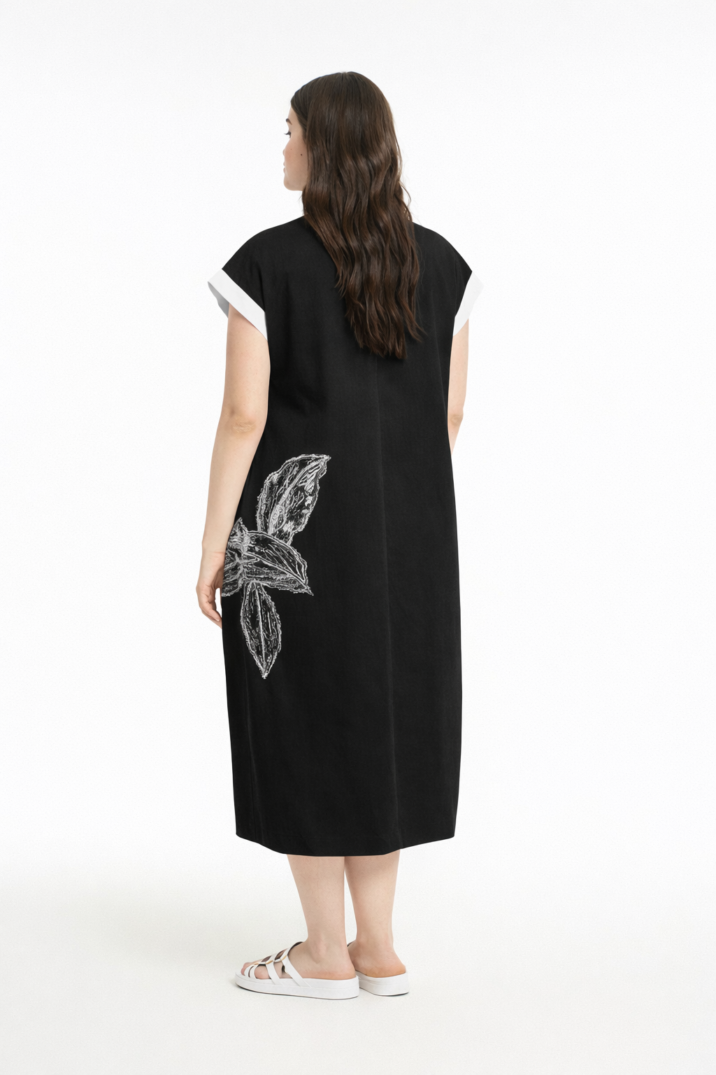 Woman wearing a black dress with a V neckline, short sleeves, midi length and white floral design on a white background