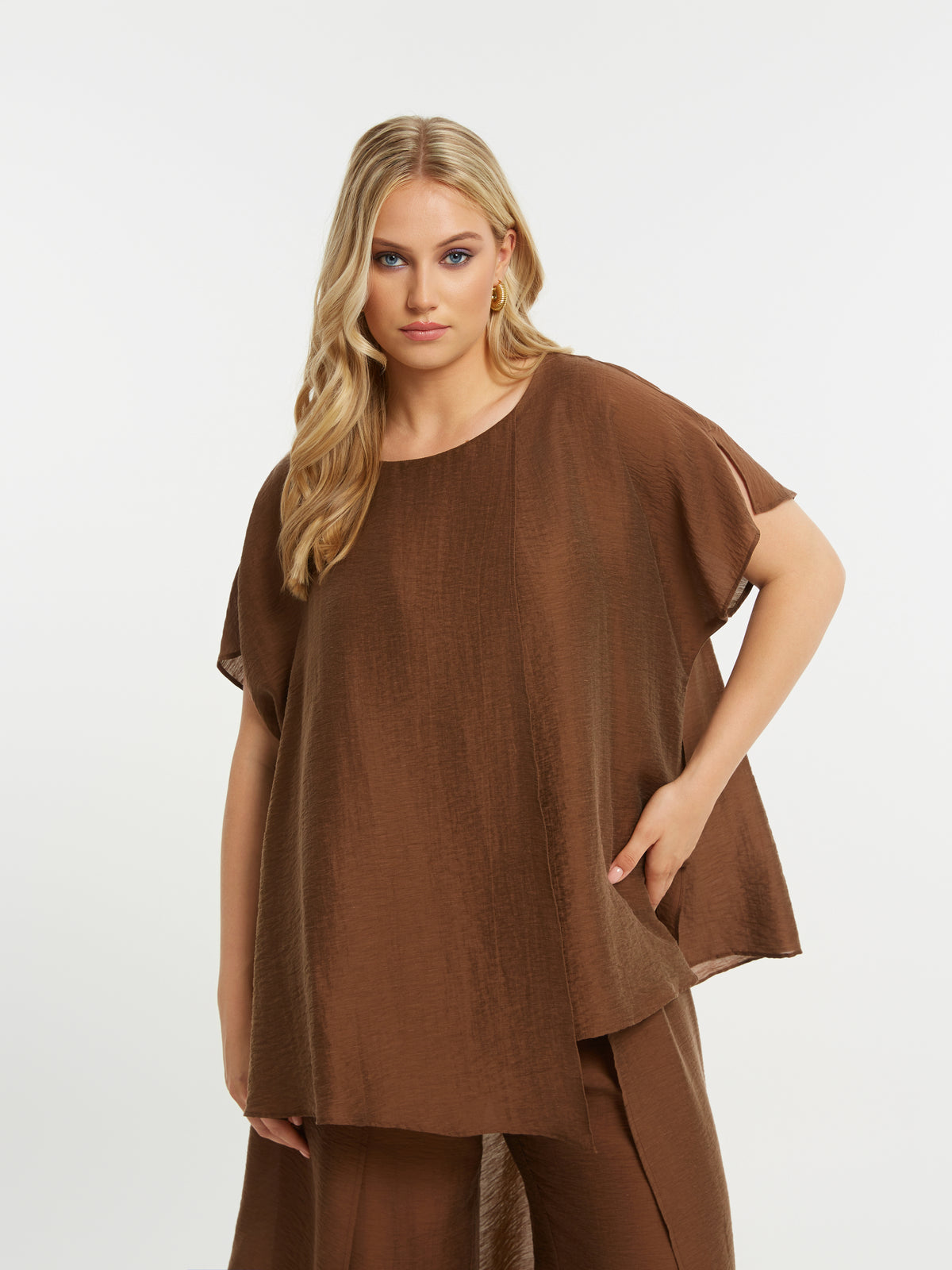 Woman wearing a brown Top and trousers against a white background