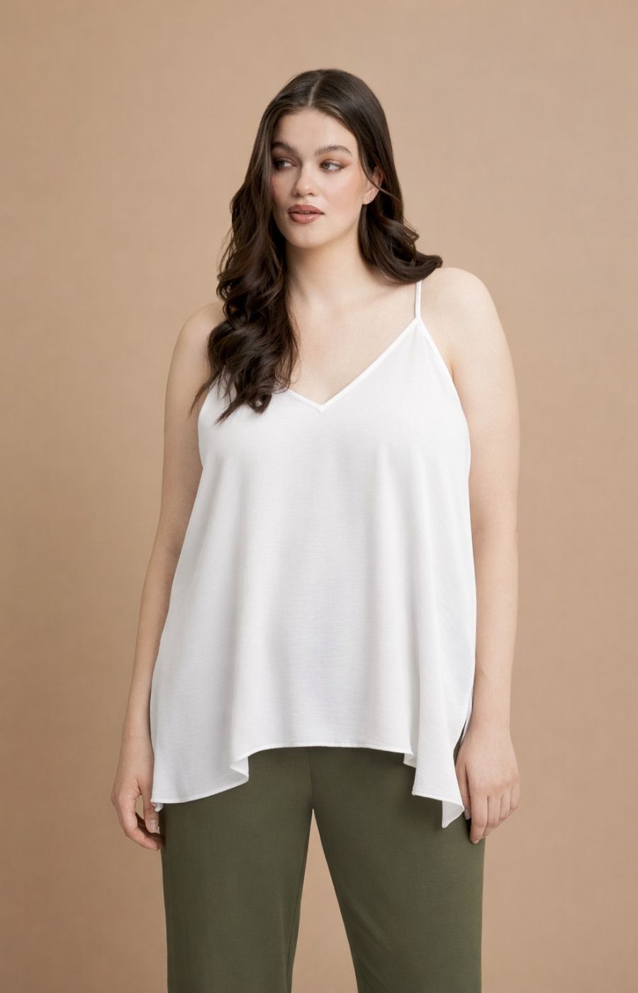 Woman wearing the Mat Cami in White, a white sleeveless top and green pants on a beige background