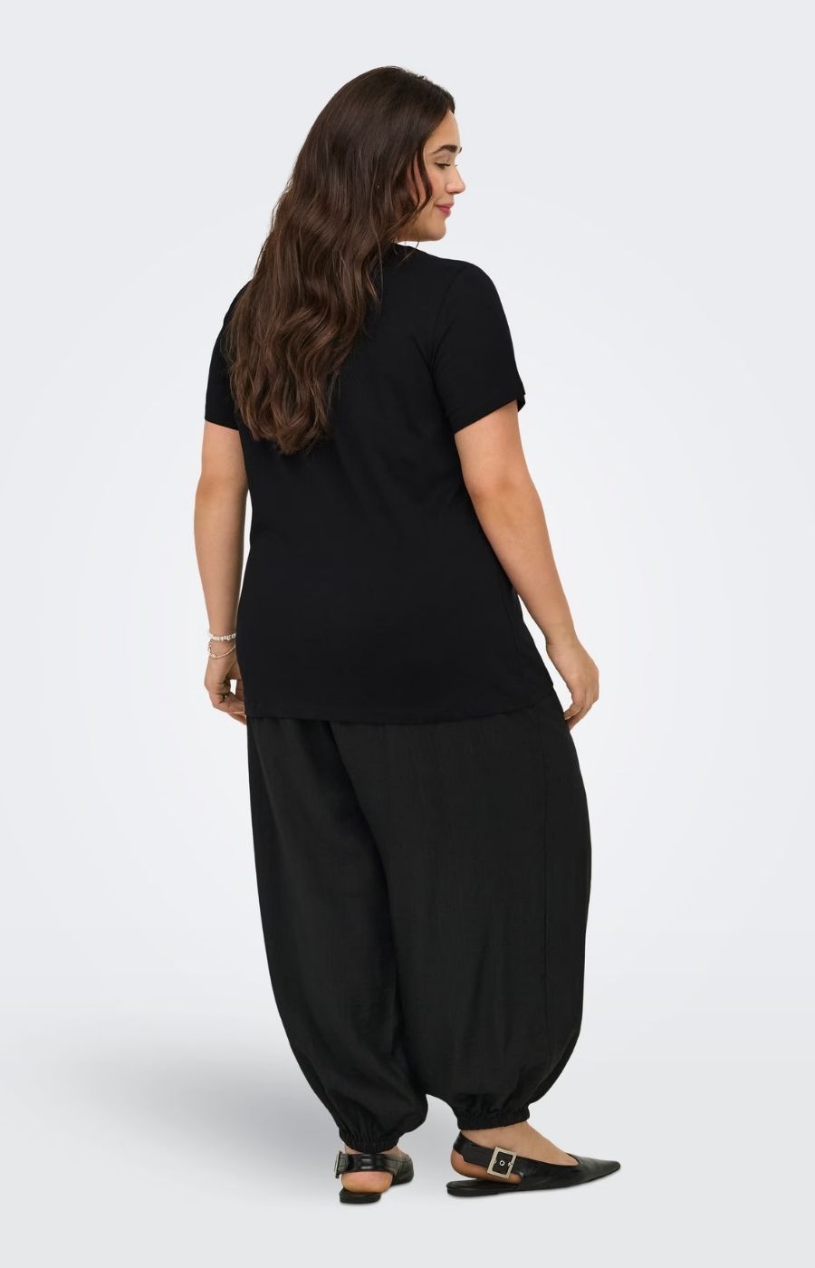 Woman wearing the Only Carmakoma Beau T-Shirt in Black with wide-leg pants on a white background. This image was created using AI.