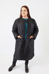 Person wearing a long black quilted coat on a white background