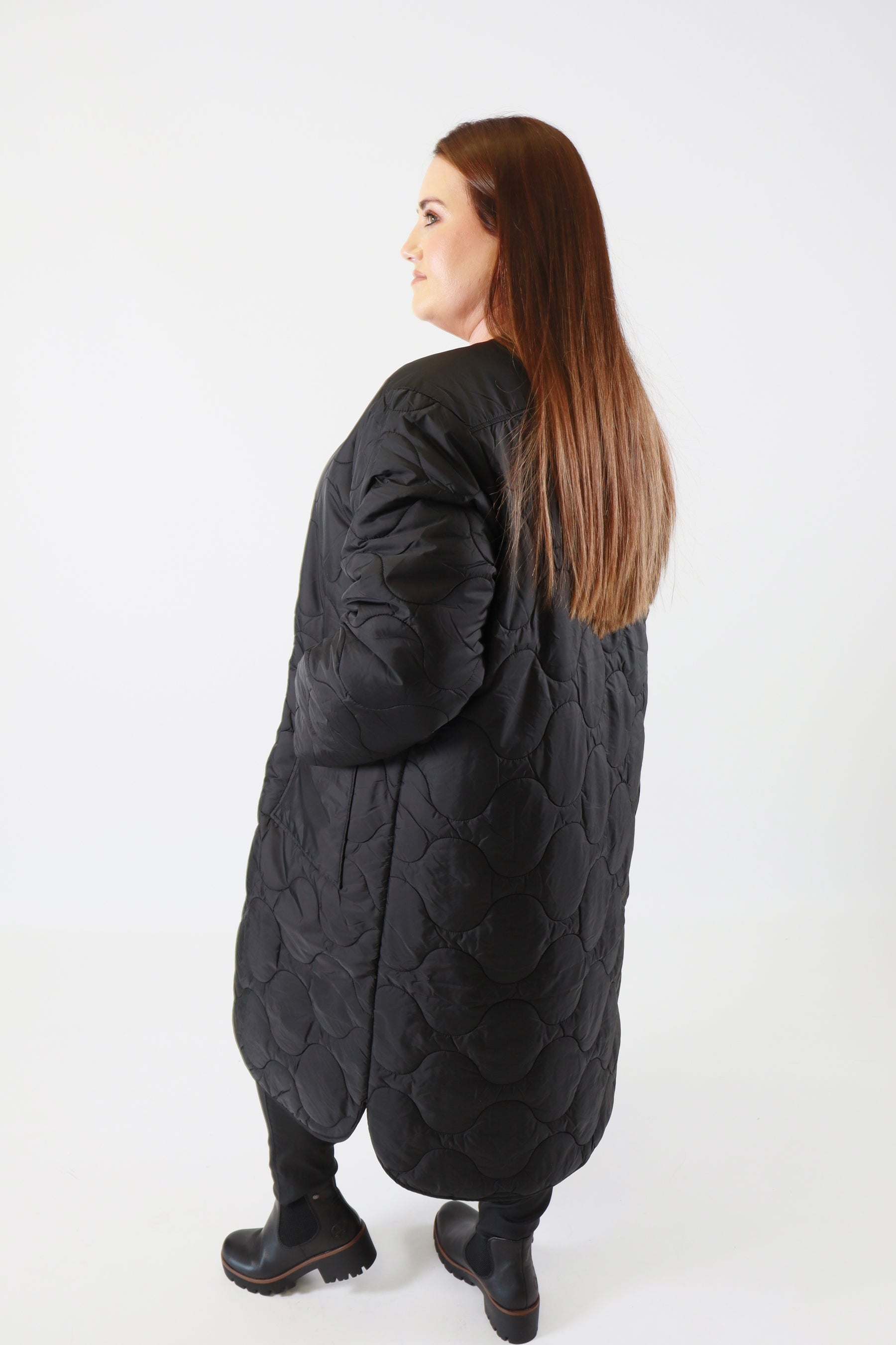 Person wearing a long black quilted coat on a white background