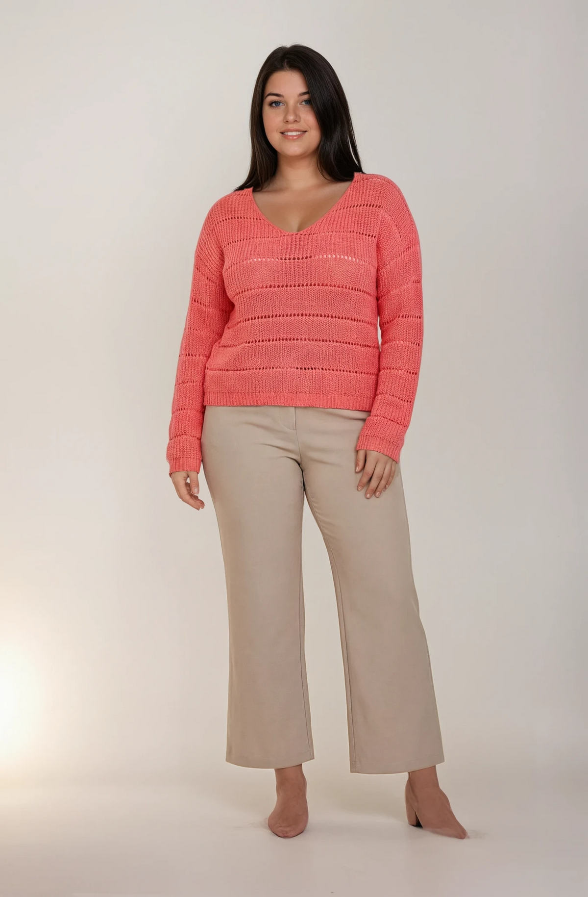 Woman wearing a pink sweater and beige pants on a white background