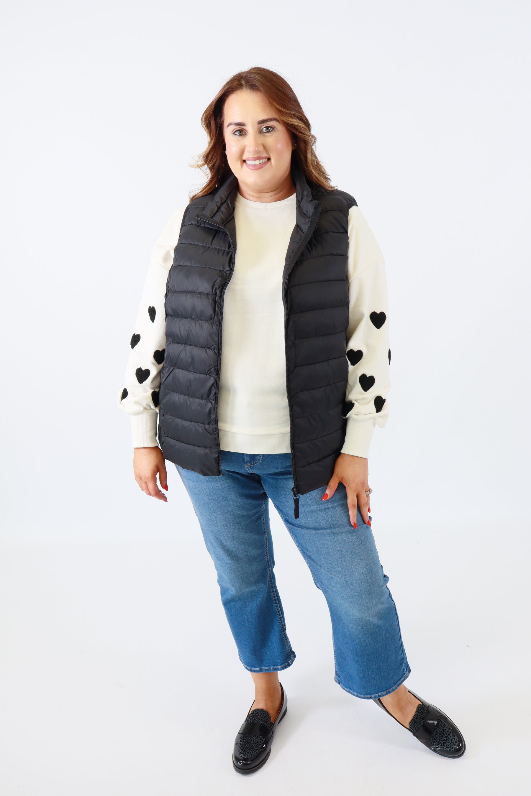 Person wearing a black puffer vest over a white shirt with blue jeans on a white background