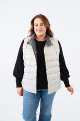 Person wearing a black sweater and white puffer vest on a white background