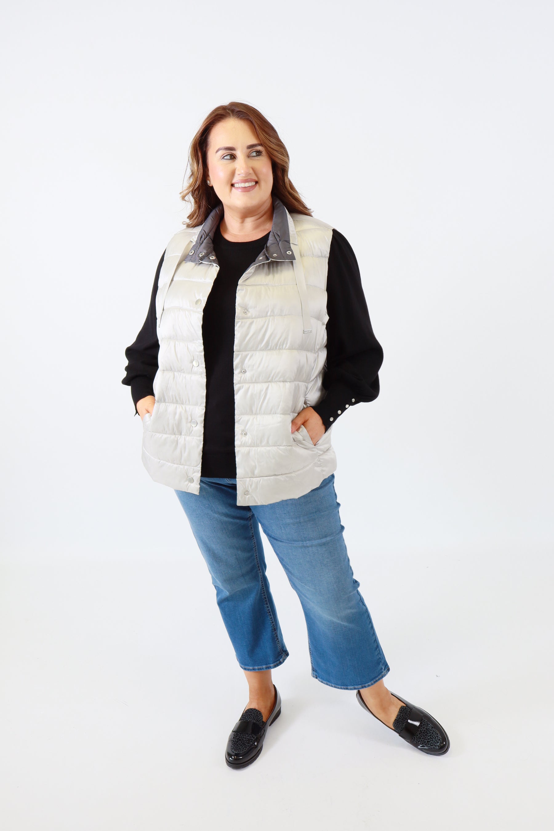 Person wearing a black jacket, white vest, blue jeans, and black shoes on a white background