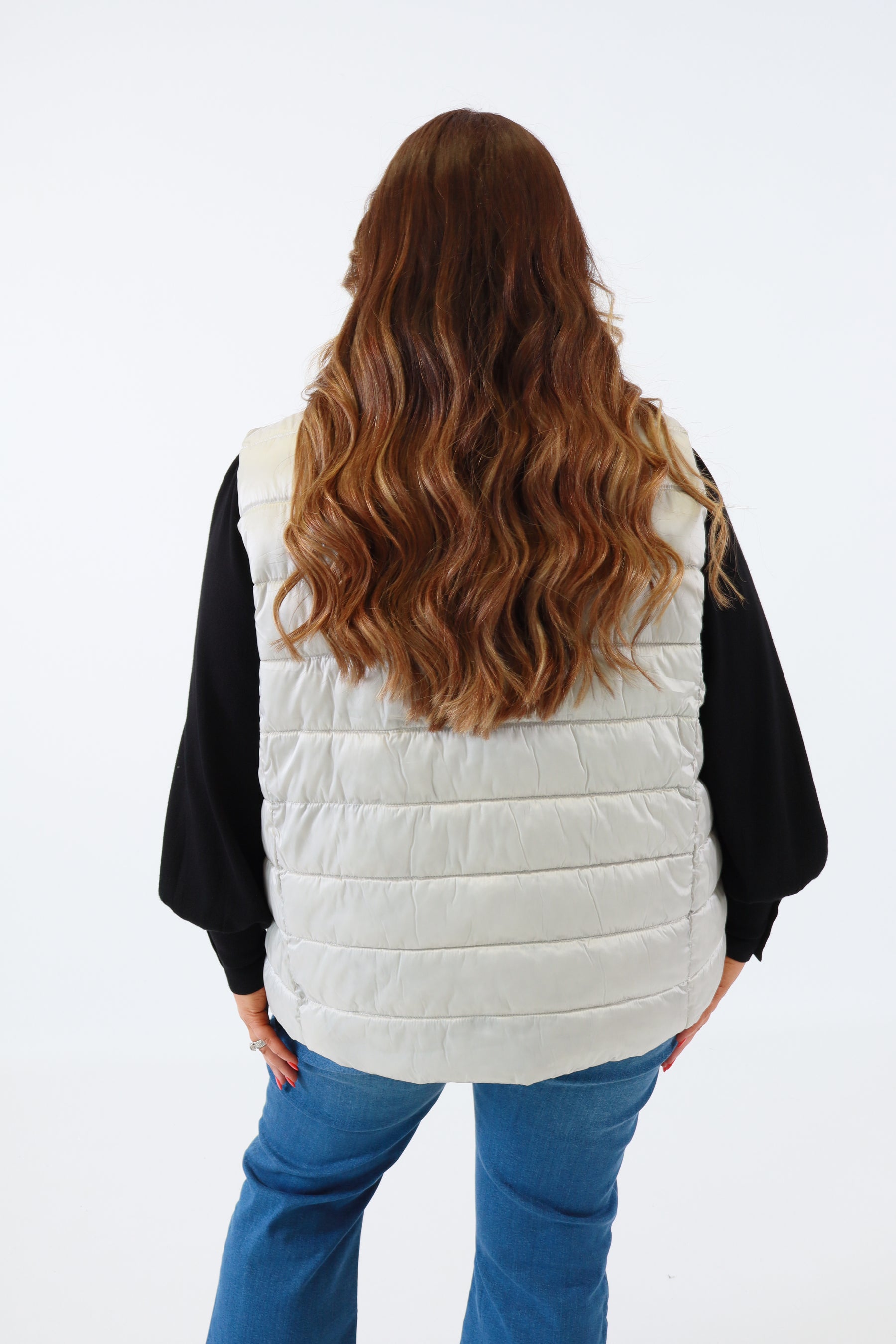 Person wearing a silver puffer vest over a black jacket on a white background
