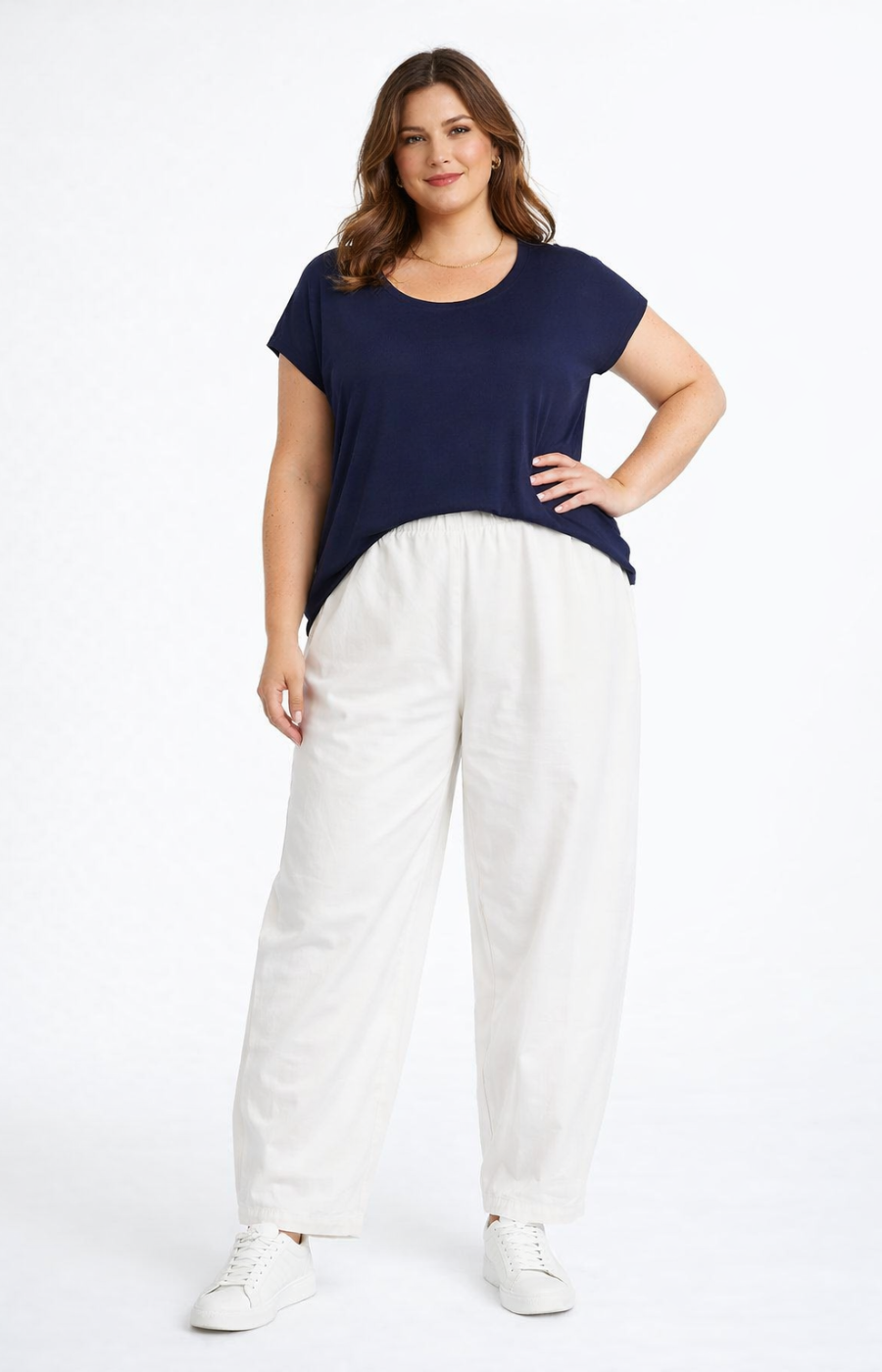 Woman wearing a navy top and white pants on a white background