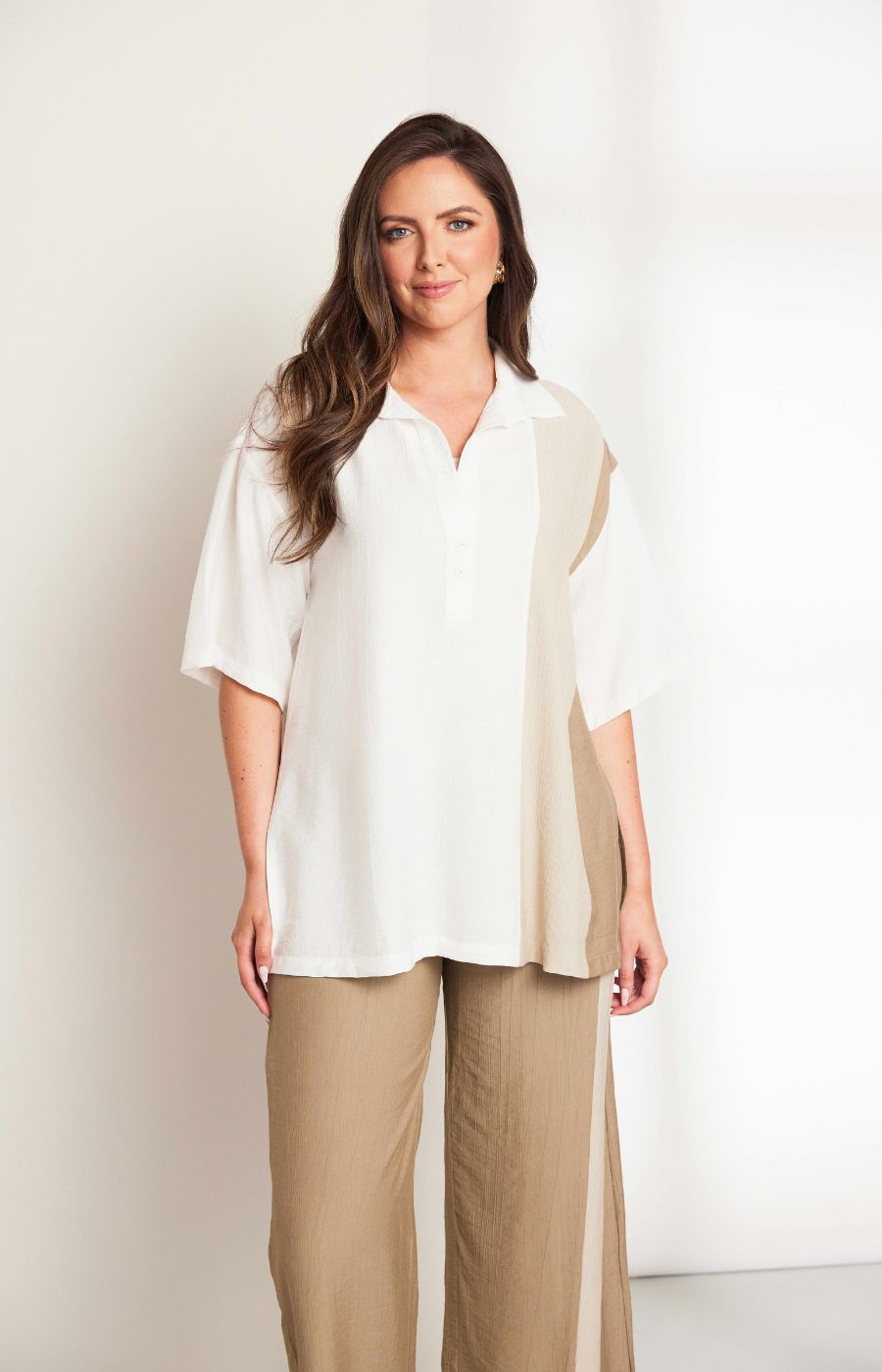 Woman wearing the Ora Crinkle Top with Collar in Beige, a white top with a beige side stripe down the front and back, a collard V neckline, short sleeves and side slits, worn with beige pants against a plain background