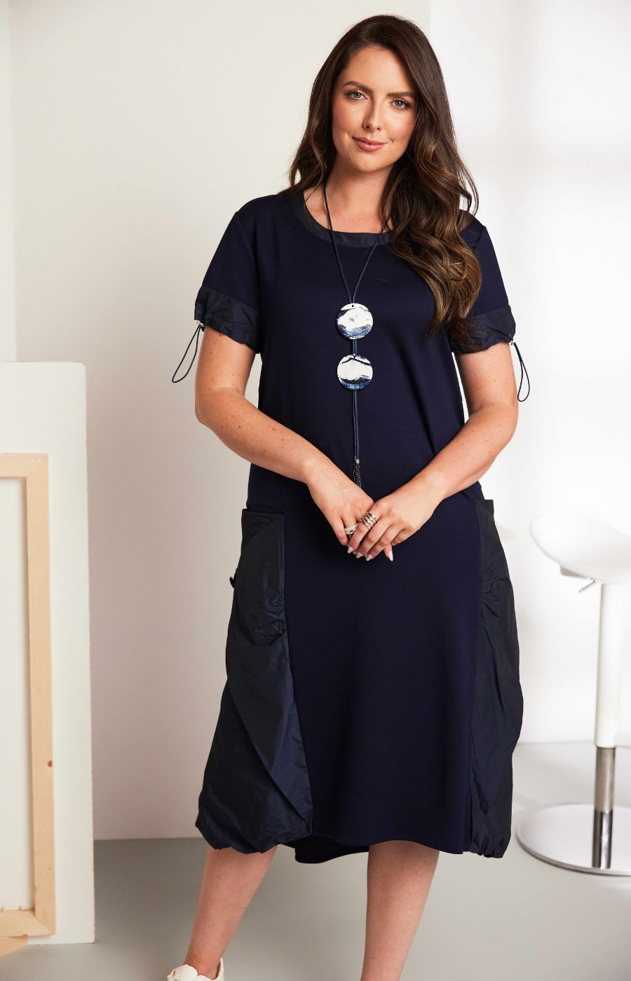 Woman wearing the Ora Side Pocket Dress in Navy, a navy blue dress with side pockets, round neckline and short sleeves, in a midi length.