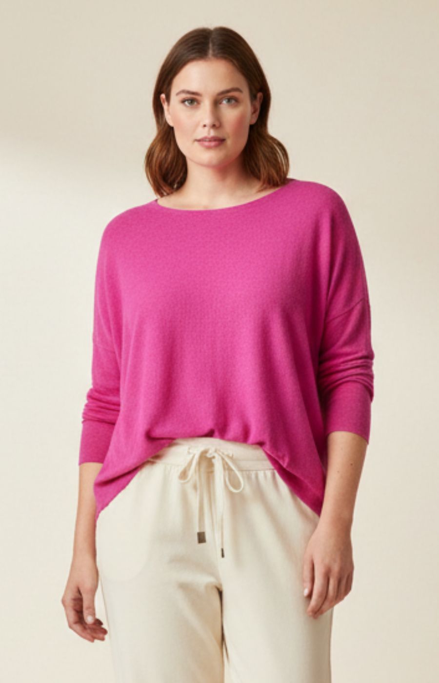Woman wearing a bright pink sweater and beige pants on a plain background