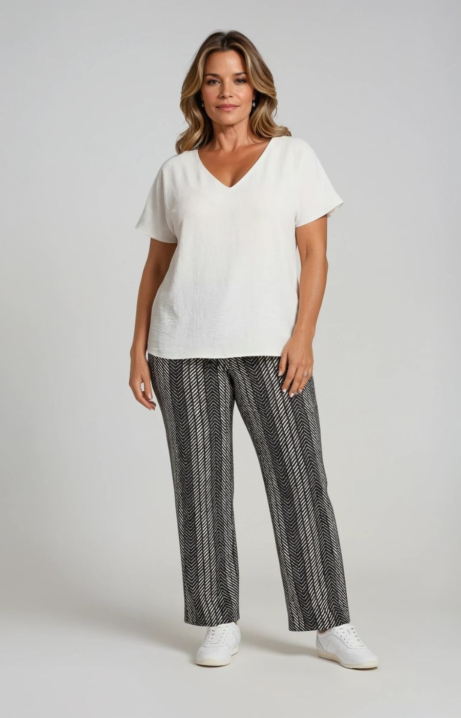 Woman wearing a white top and patterned pants on a plain background