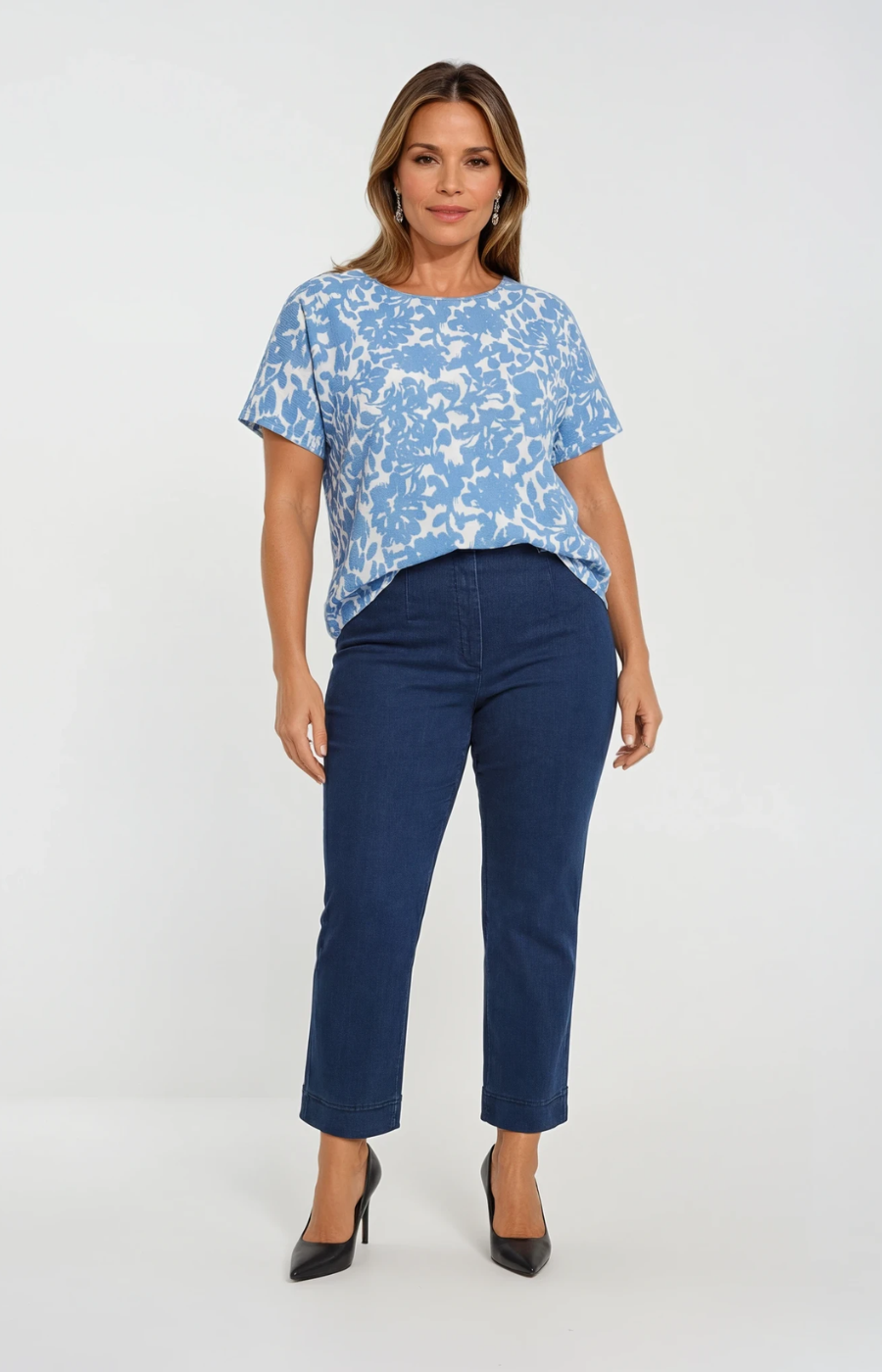 Woman wearing a blue patterned top and dark blue jeans on a white background