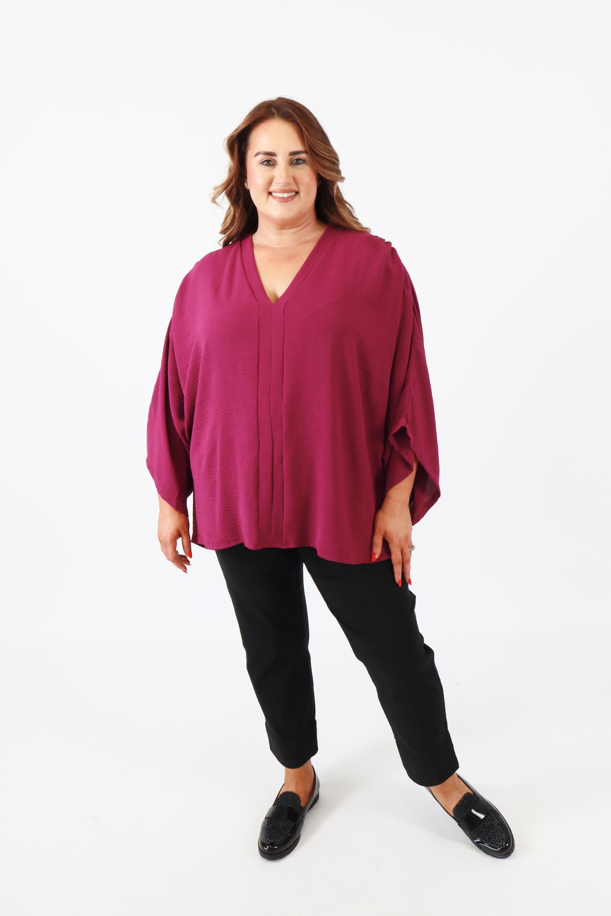 Woman wearing a magenta blouse and black pants on a white background