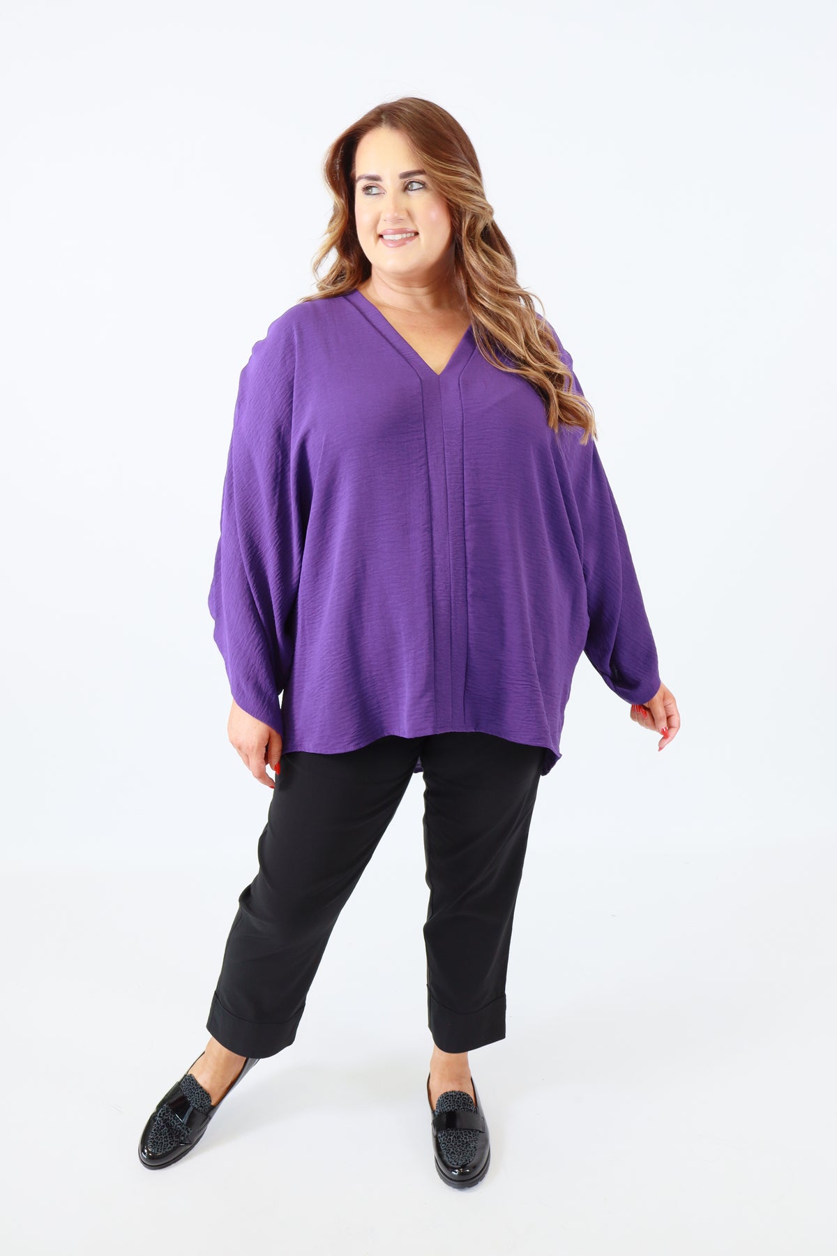 Person wearing a purple top and black pants on a white background