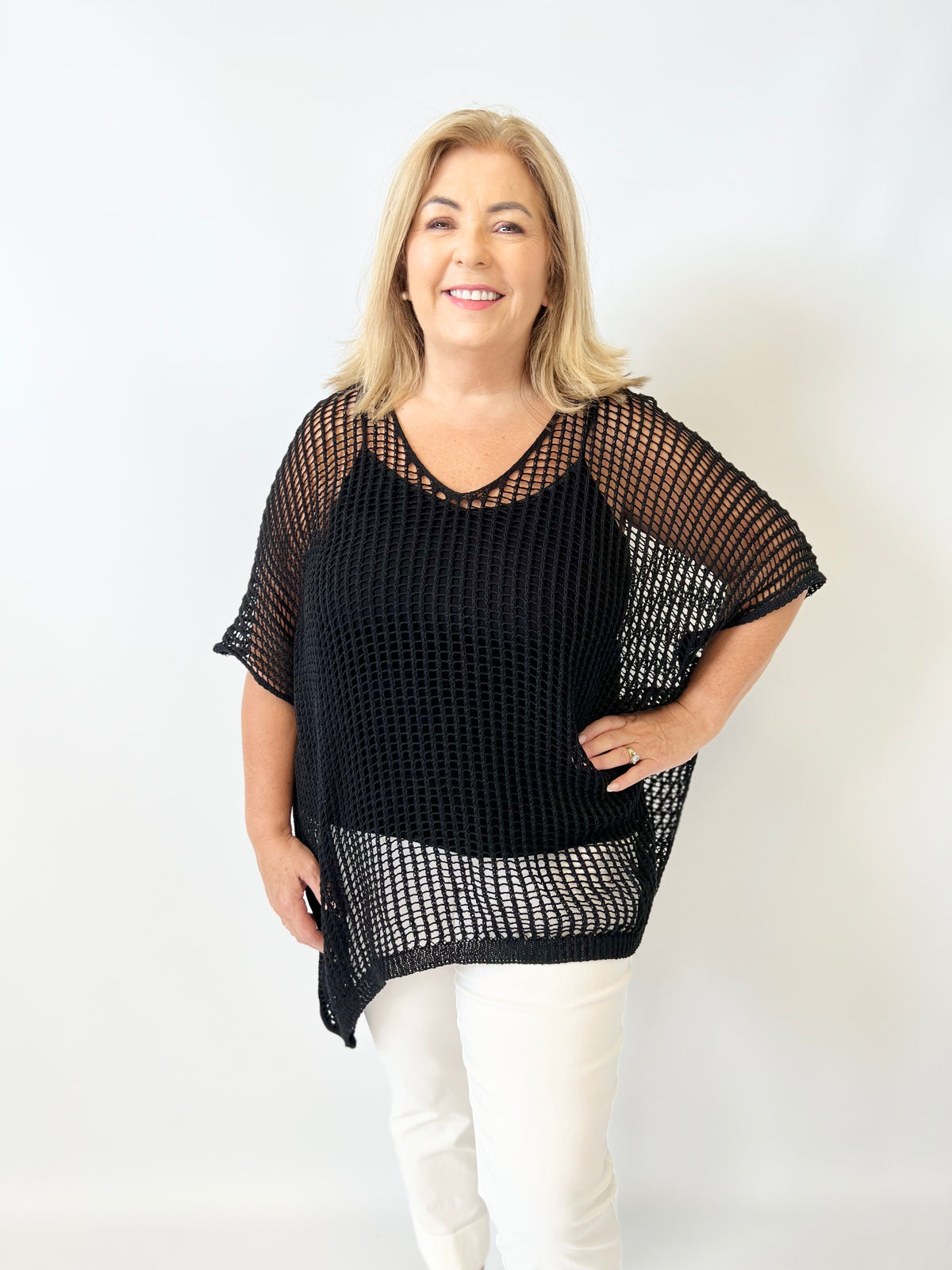 Woman wearing a black mesh top and white pants on a white background