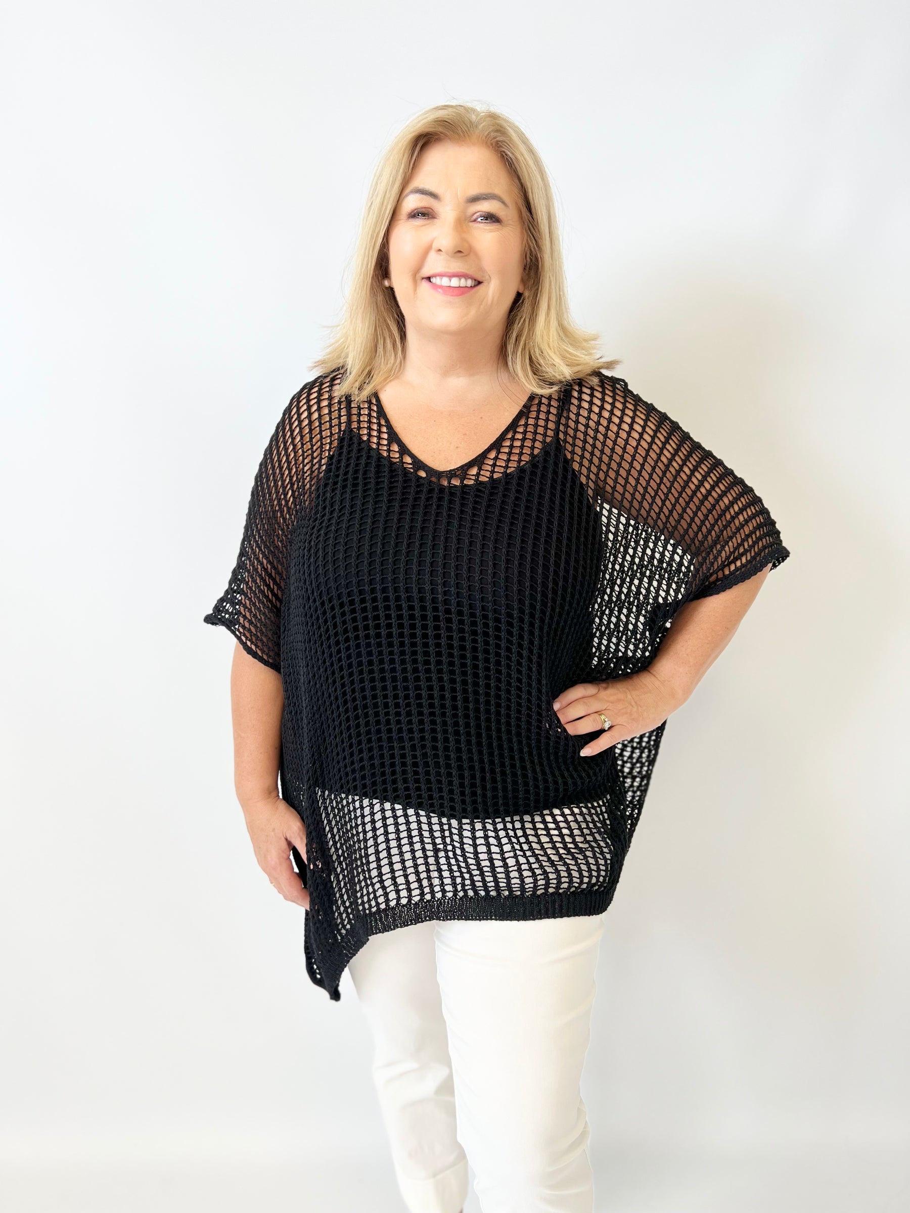 Woman wearing a black mesh top and white pants on a white background