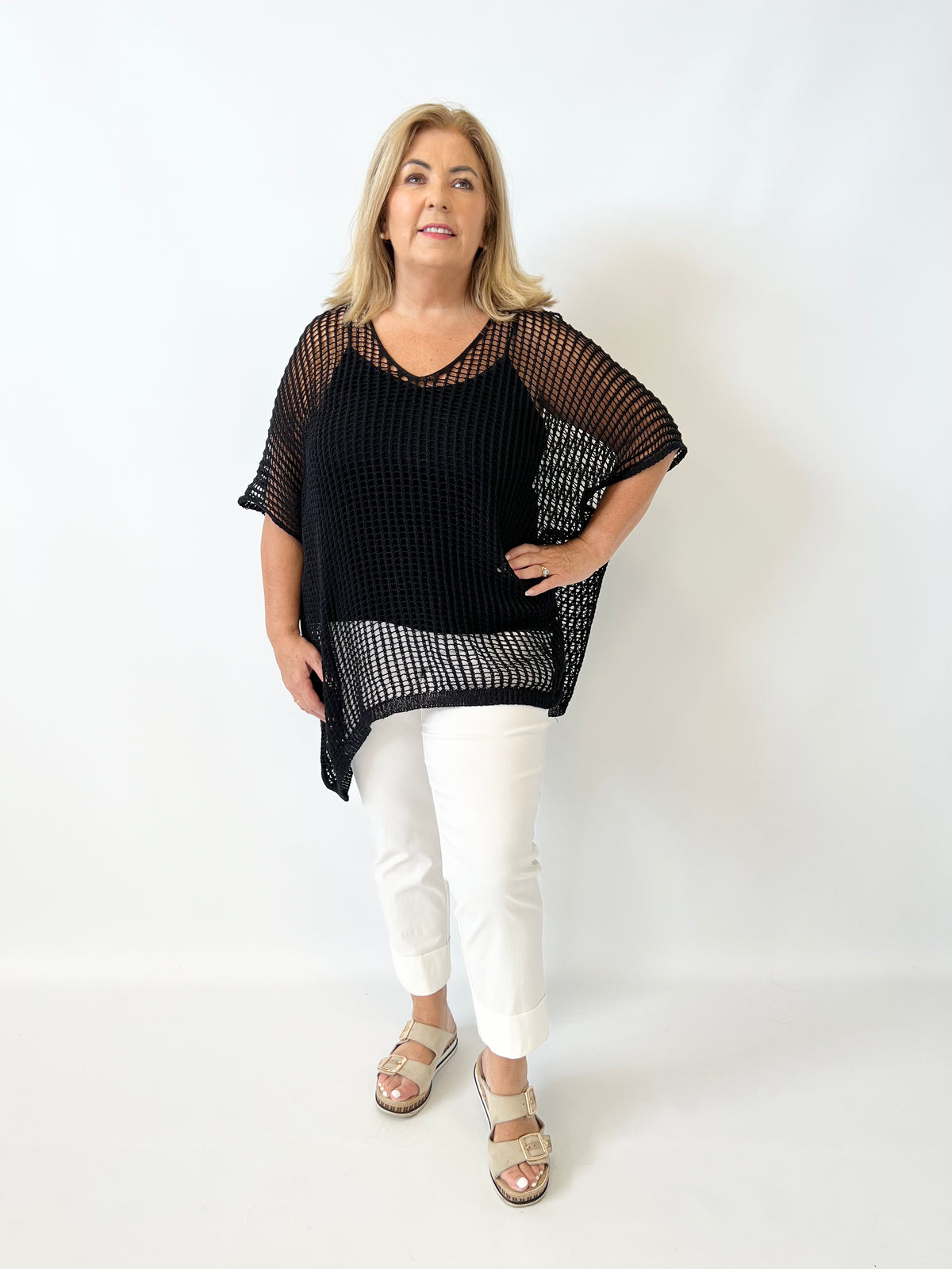 Woman wearing a black knit top and white pants on a white background