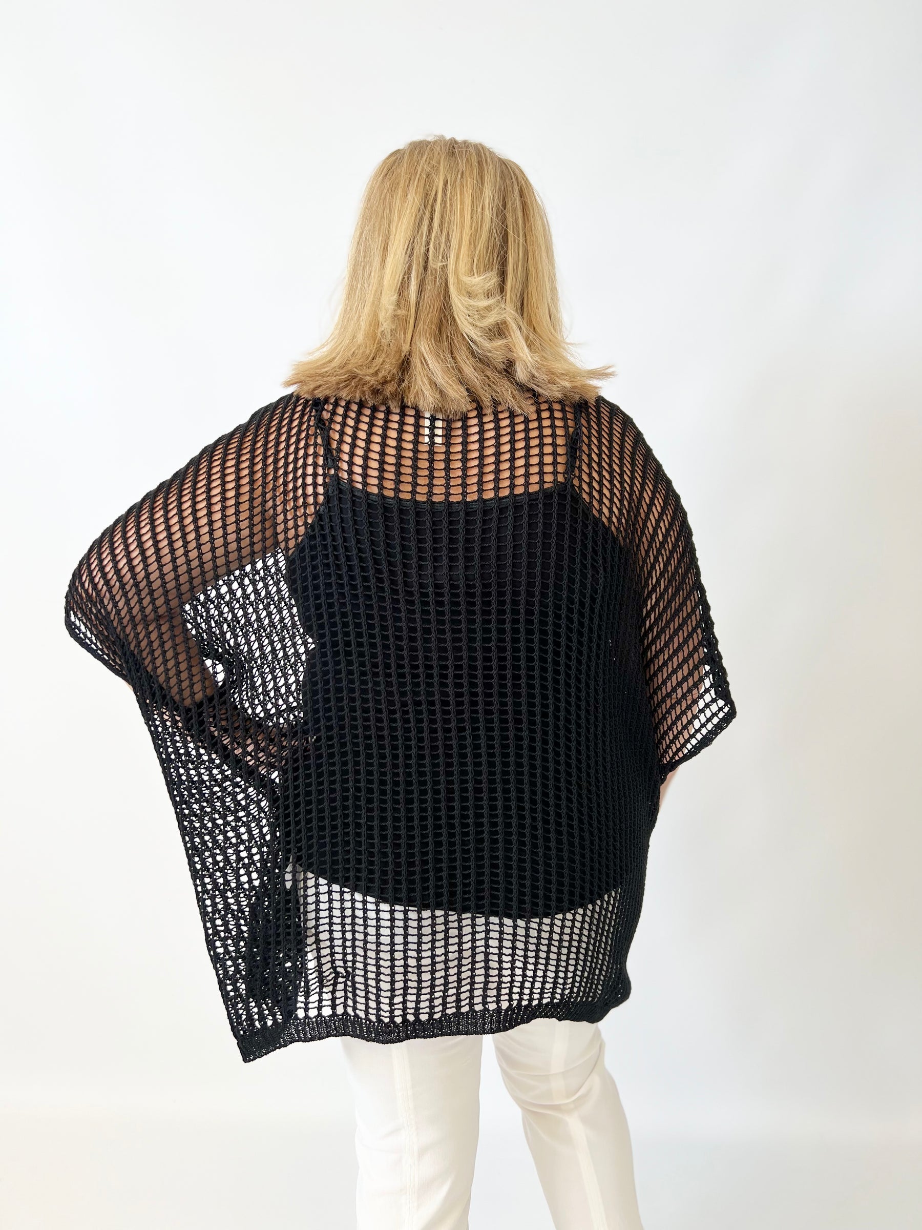 Person wearing a black knit poncho with sheer sides on a white background