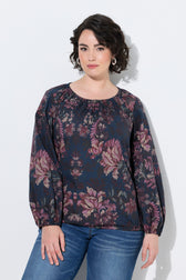 A woman modeling the Ulla Popken Floral Damask Blouse in Navy, a long-sleeve blouse with a dark navy blue base and a pink and purple floral pattern, paired with blue jeans, against a plain white background.