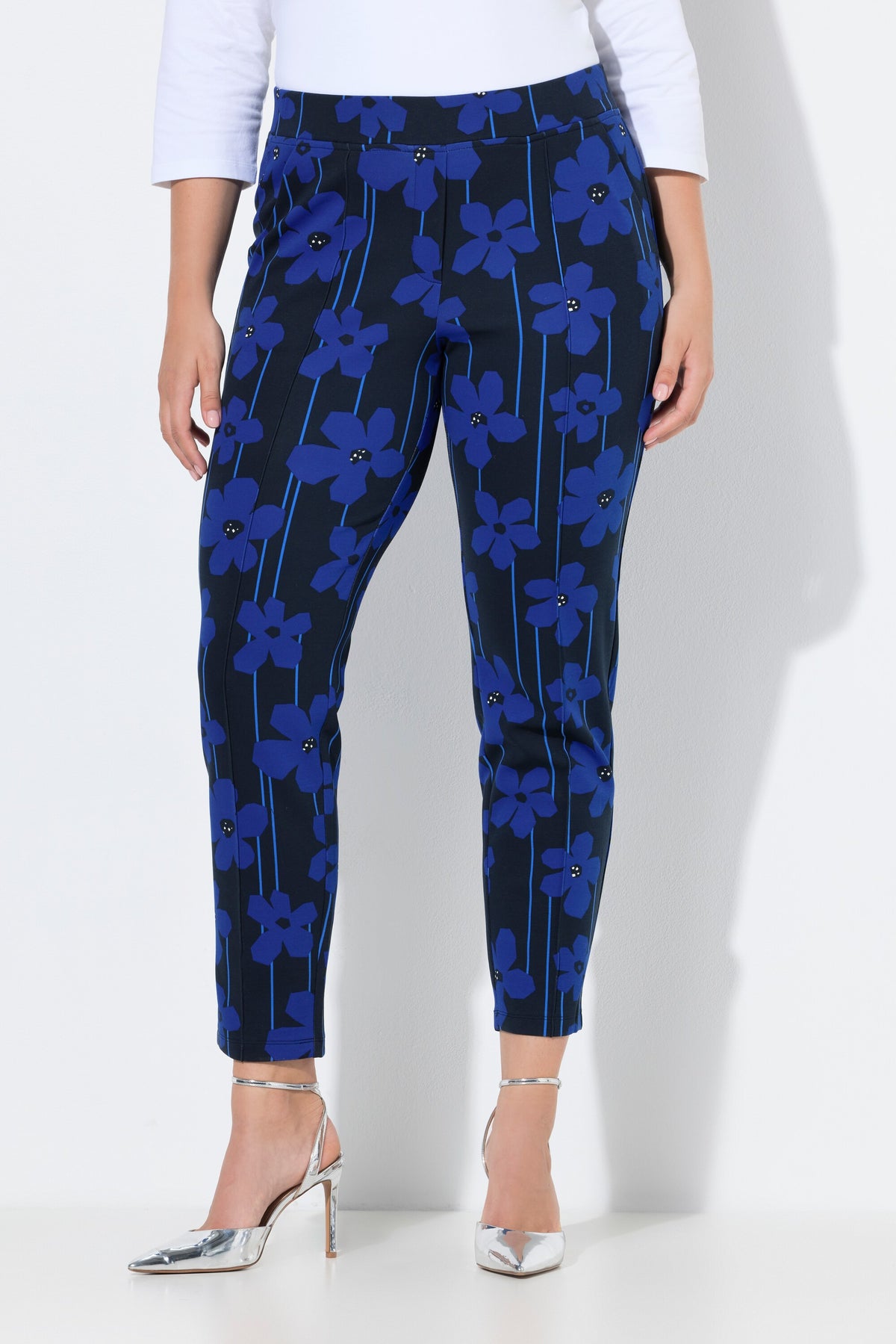 Women wearing the Ulla Popken Floral Trousers in Blue, a dark trousers with a blue floral design all over, has a tapered leg, side pocket