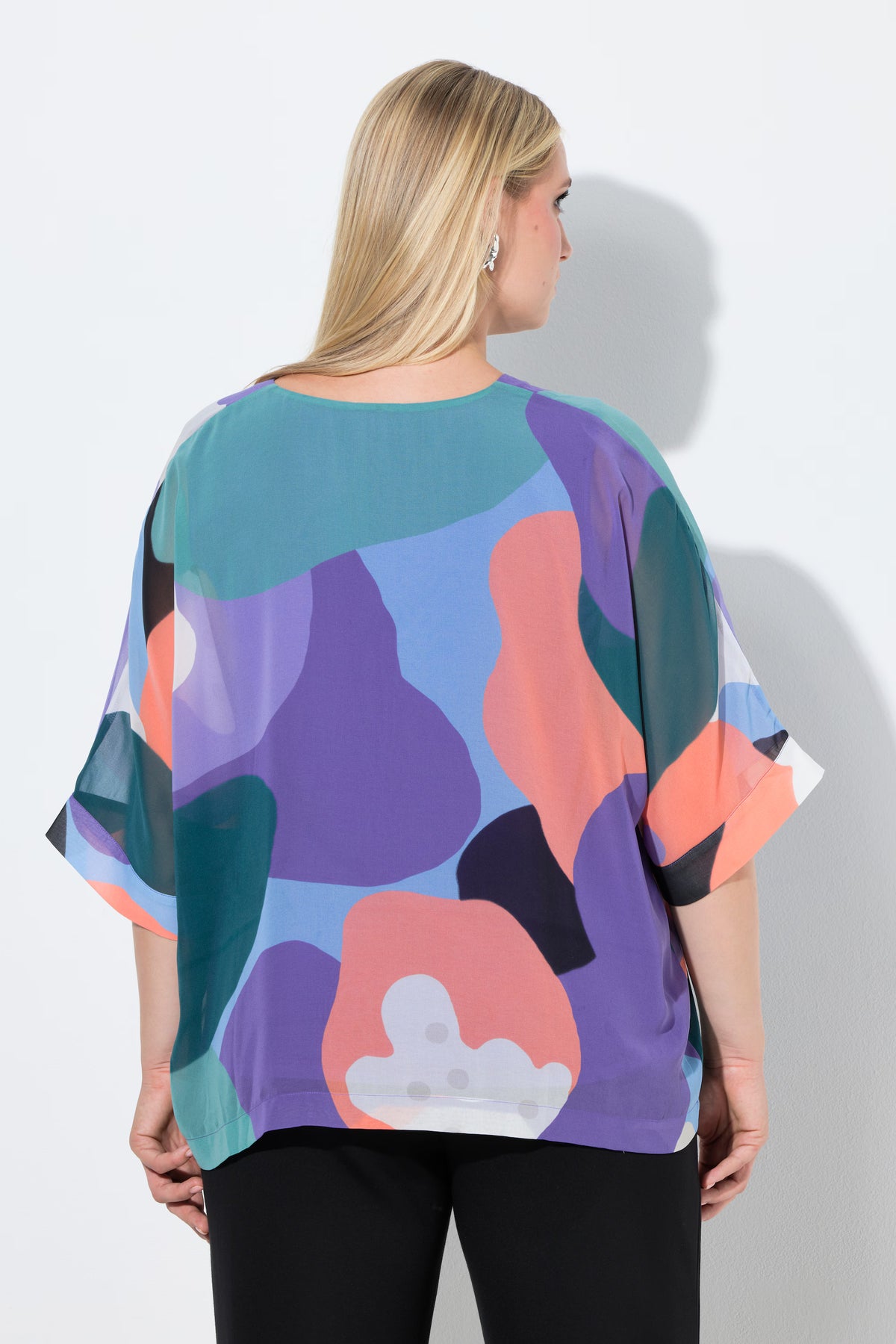 Woman wearing the Ulla Popken Multicolour Chiffon Blouse, a colorful abstract patterned top with a V neckline and 3/4 length sleeves against a white background