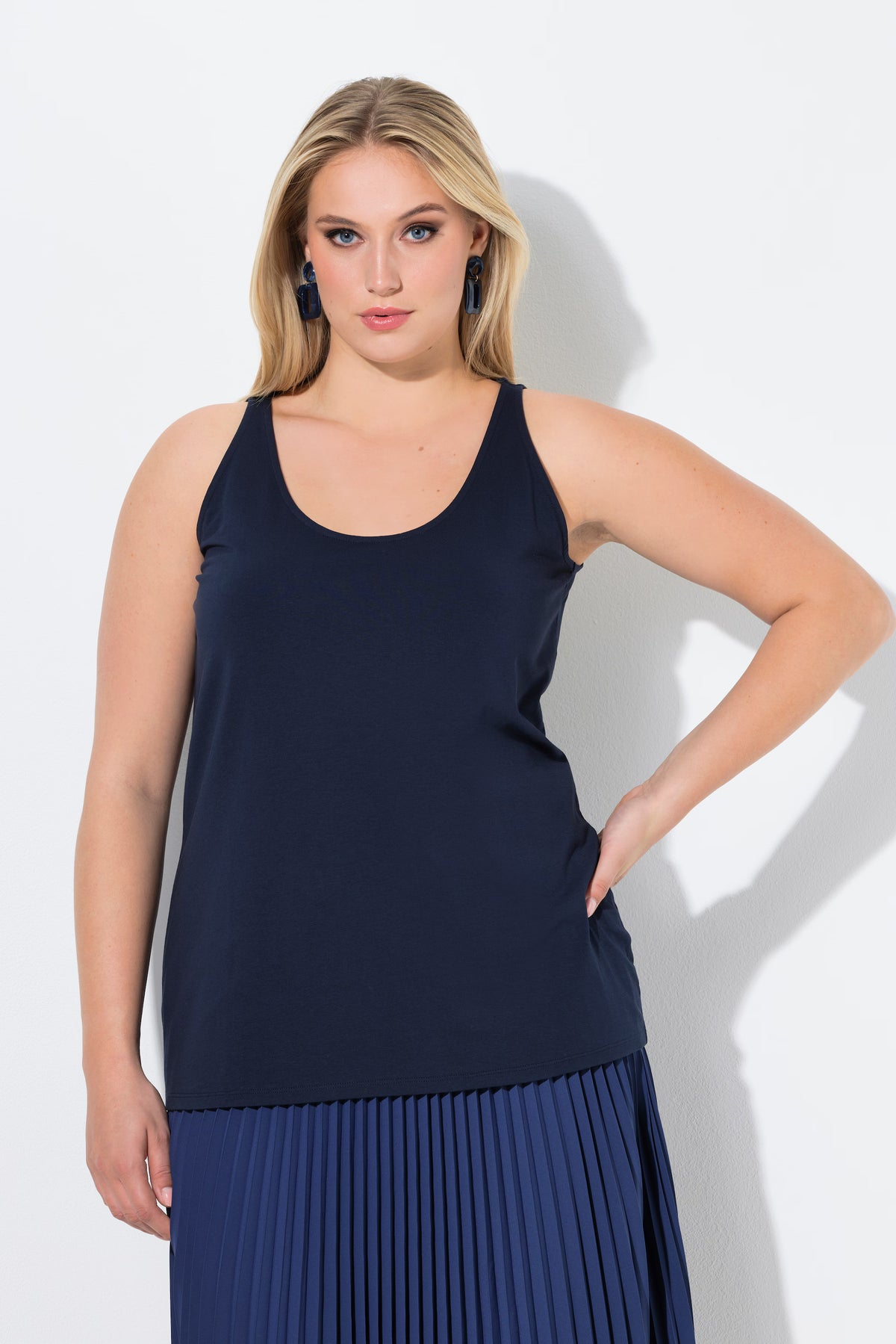 Woman wearing the Ulla Popken Vest Top in Navy, a navy blue sleeveless top with a round neckline and close fit worn with a pleated skirt on a white background