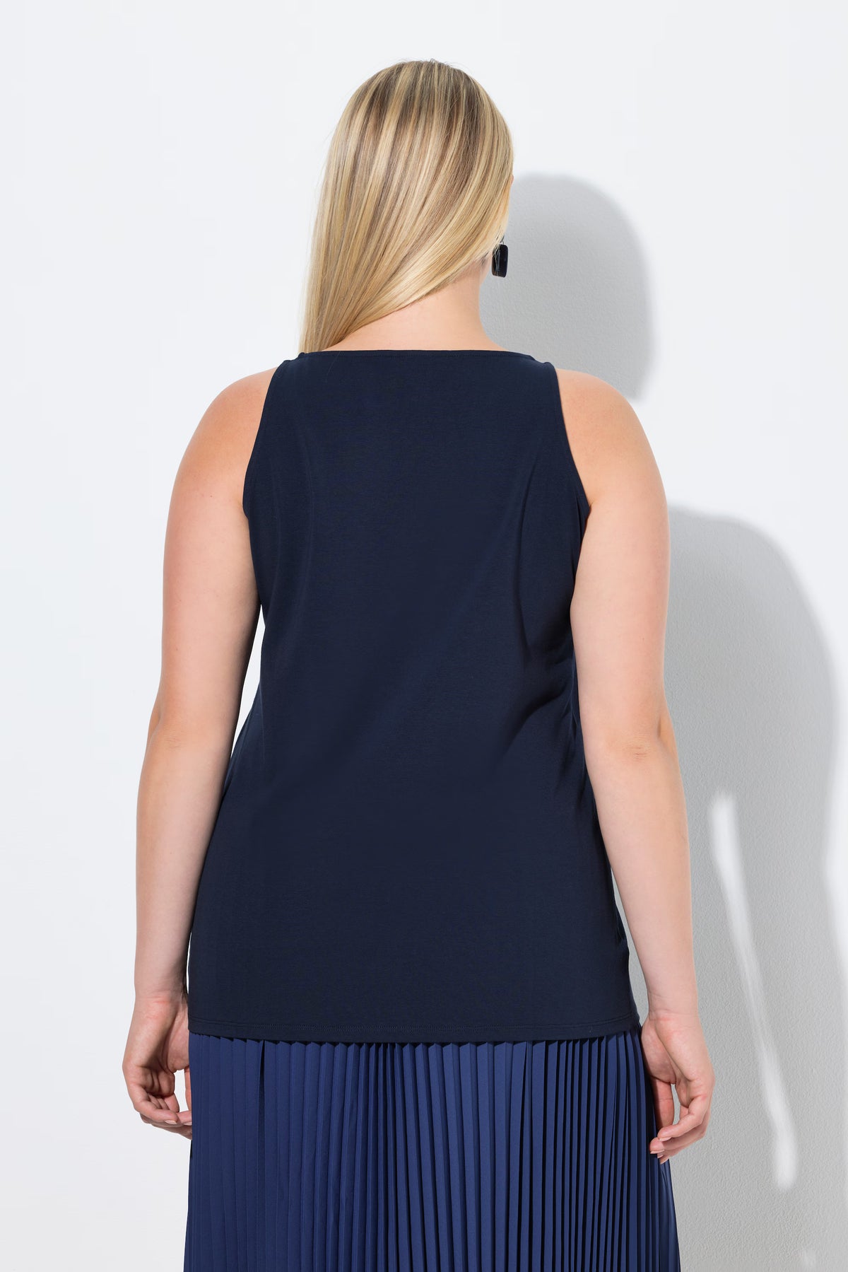 Woman wearing the Ulla Popken Vest Top in Navy, a navy blue sleeveless top with a round neckline and close fit worn with a pleated skirt on a white background