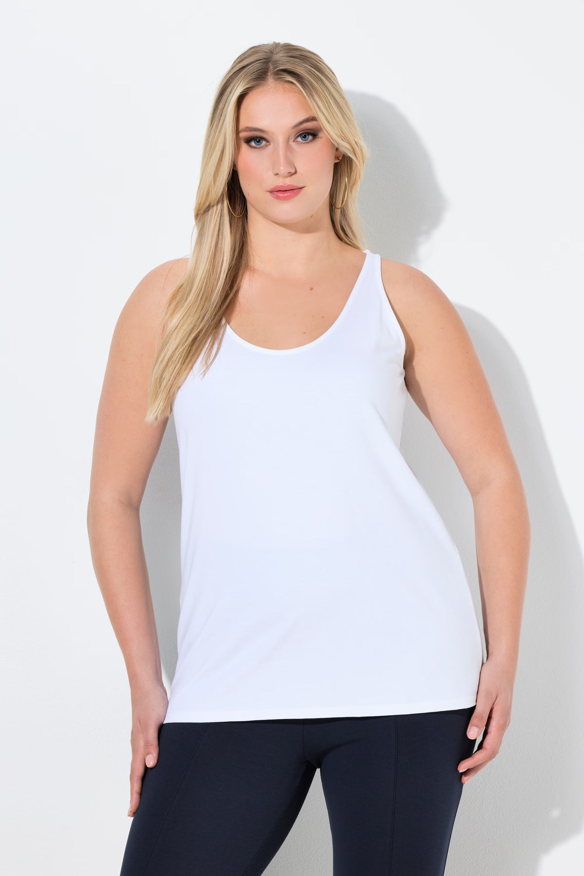 Woman wearing the Ulla Popken Vest Top in White a sleeveless top with a round neckline worn with black leggings against a white background