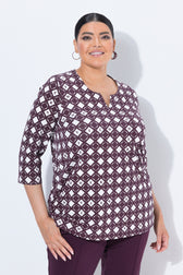 A woman modeling the Ulla Popken Wine Print Blouse, a three-quarter sleeve top with a dark purple and white geometric diamond pattern, paired with matching dark purple pants, against a light gray studio background.