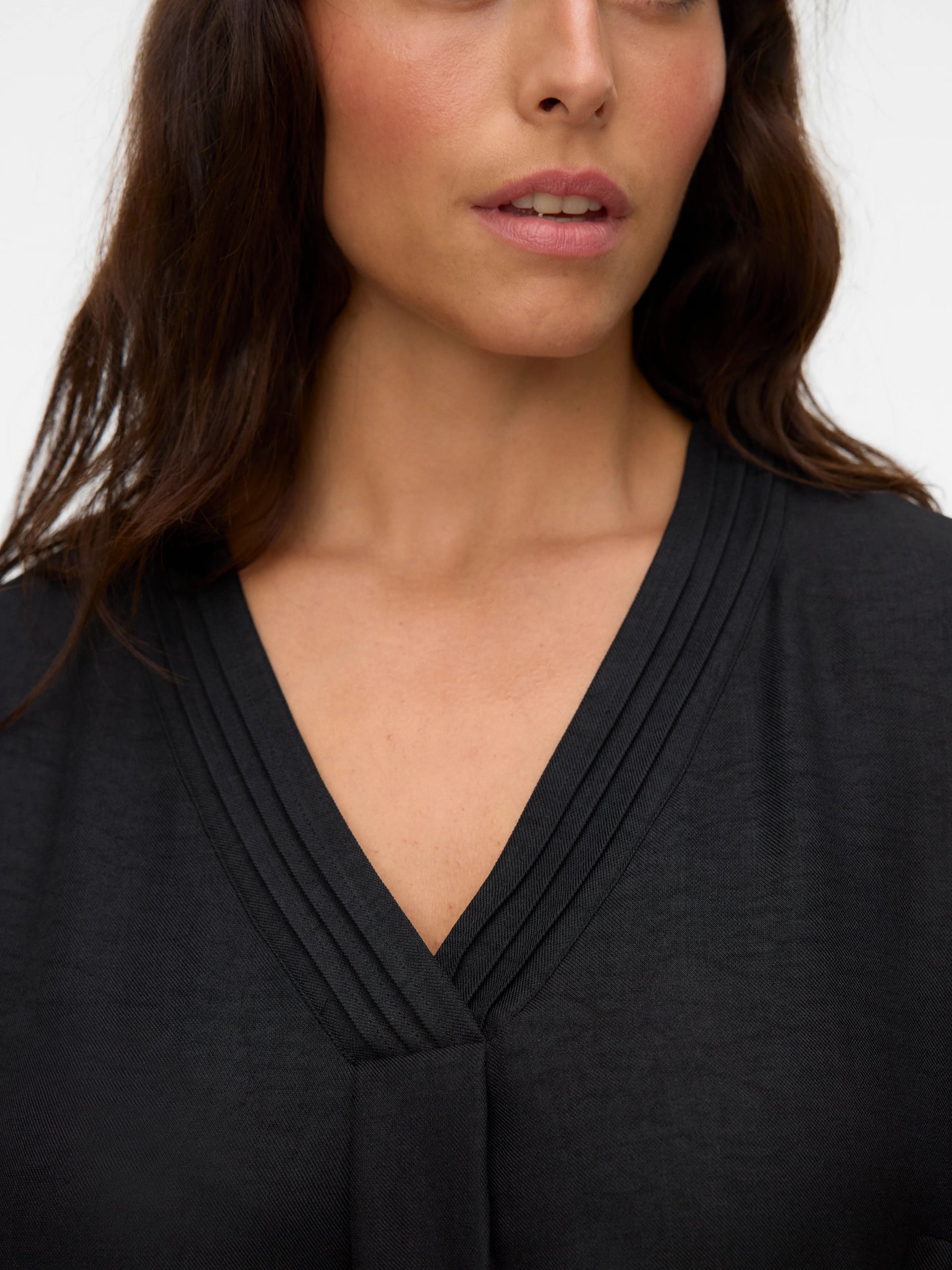 Close-up of a person wearing a black top with a V-neckline on a white background