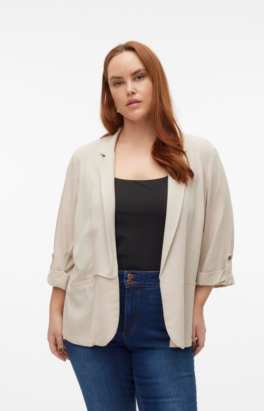 Woman wearing a beige open front blazer, black top, and blue jeans on a white background